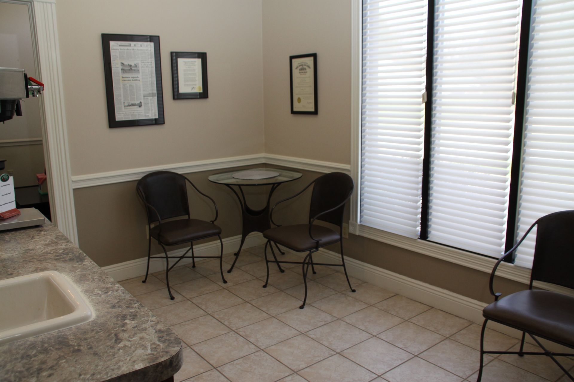 Small dining nook with two chairs, a table, framed wall art, and bright windows with blinds