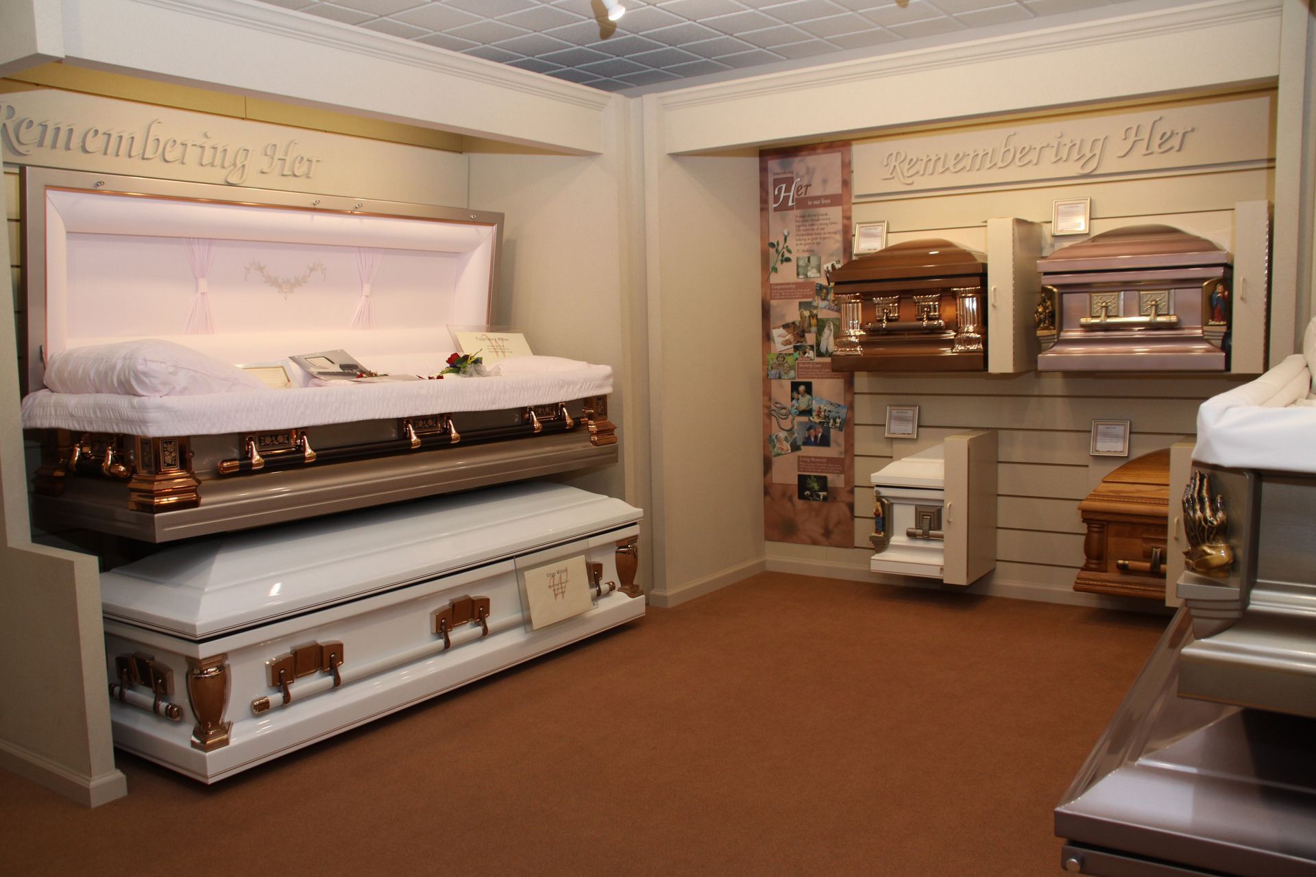 Display room with white and bronze caskets, urns, and funeral accessories on shelves and stands