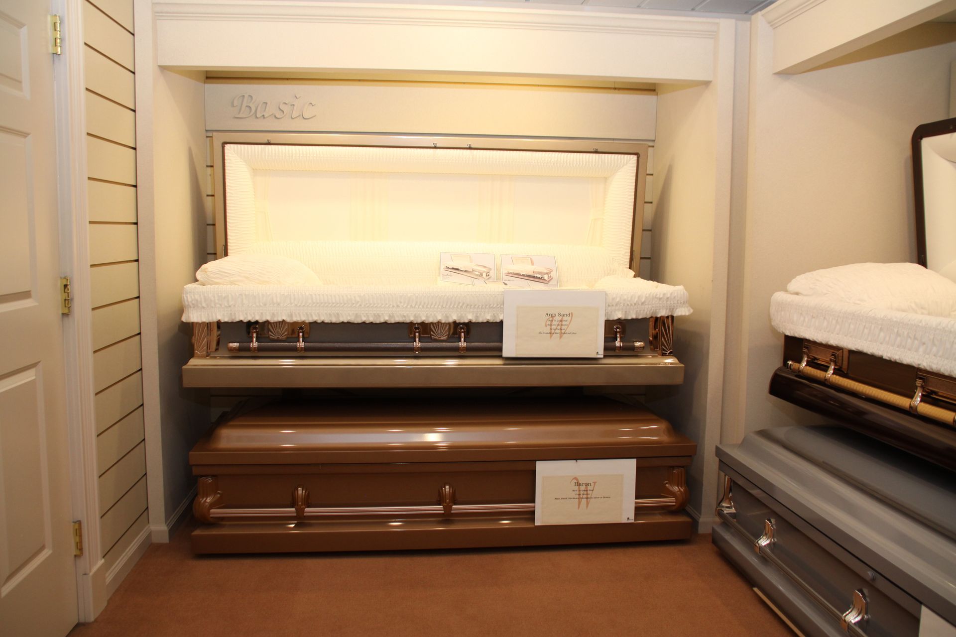 Closed caskets displayed in a funeral home showroom, with white and brown finishes.