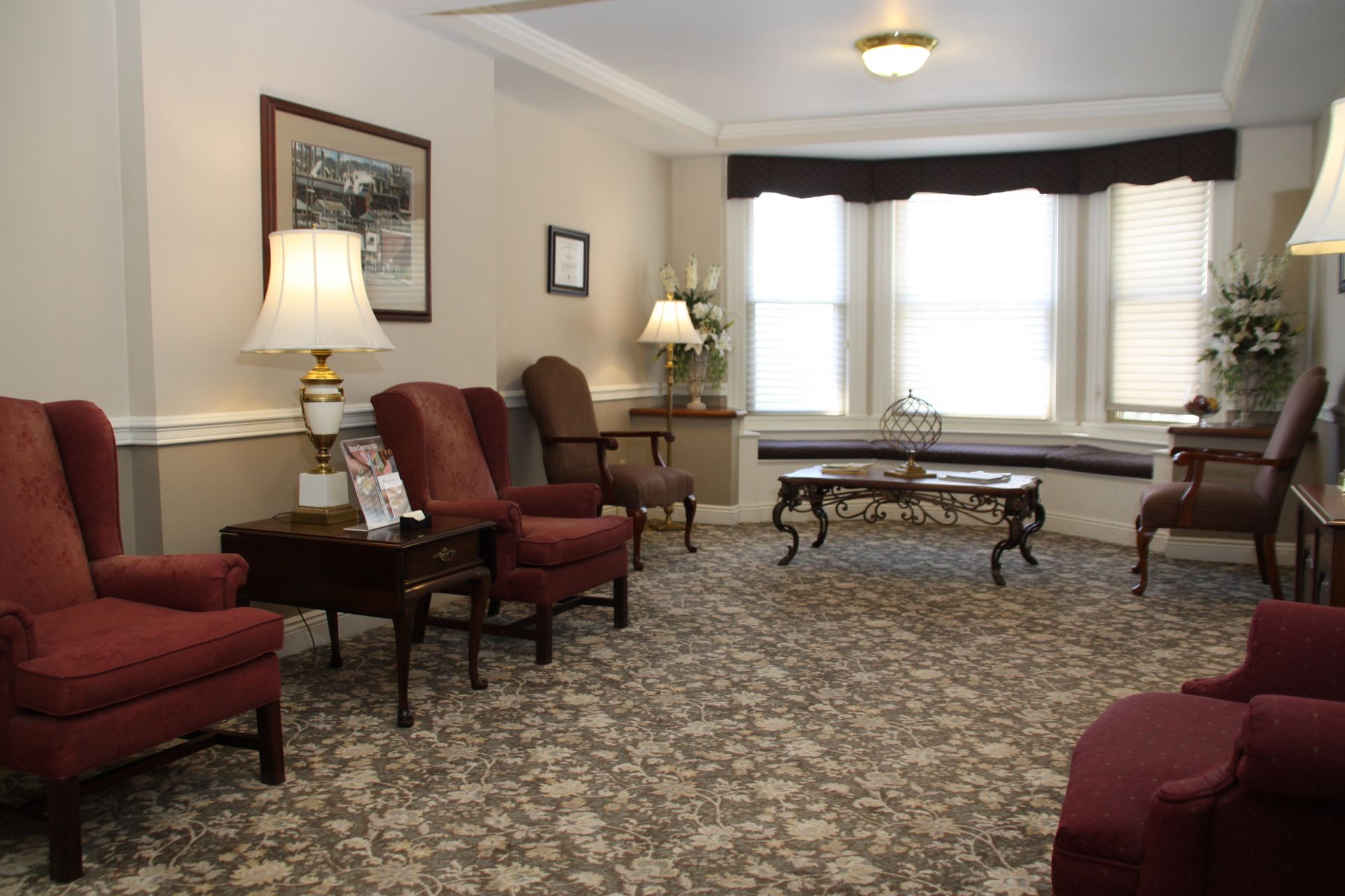 Cozy living room with red chairs, patterned carpet, bay window, lamp, and coffee table