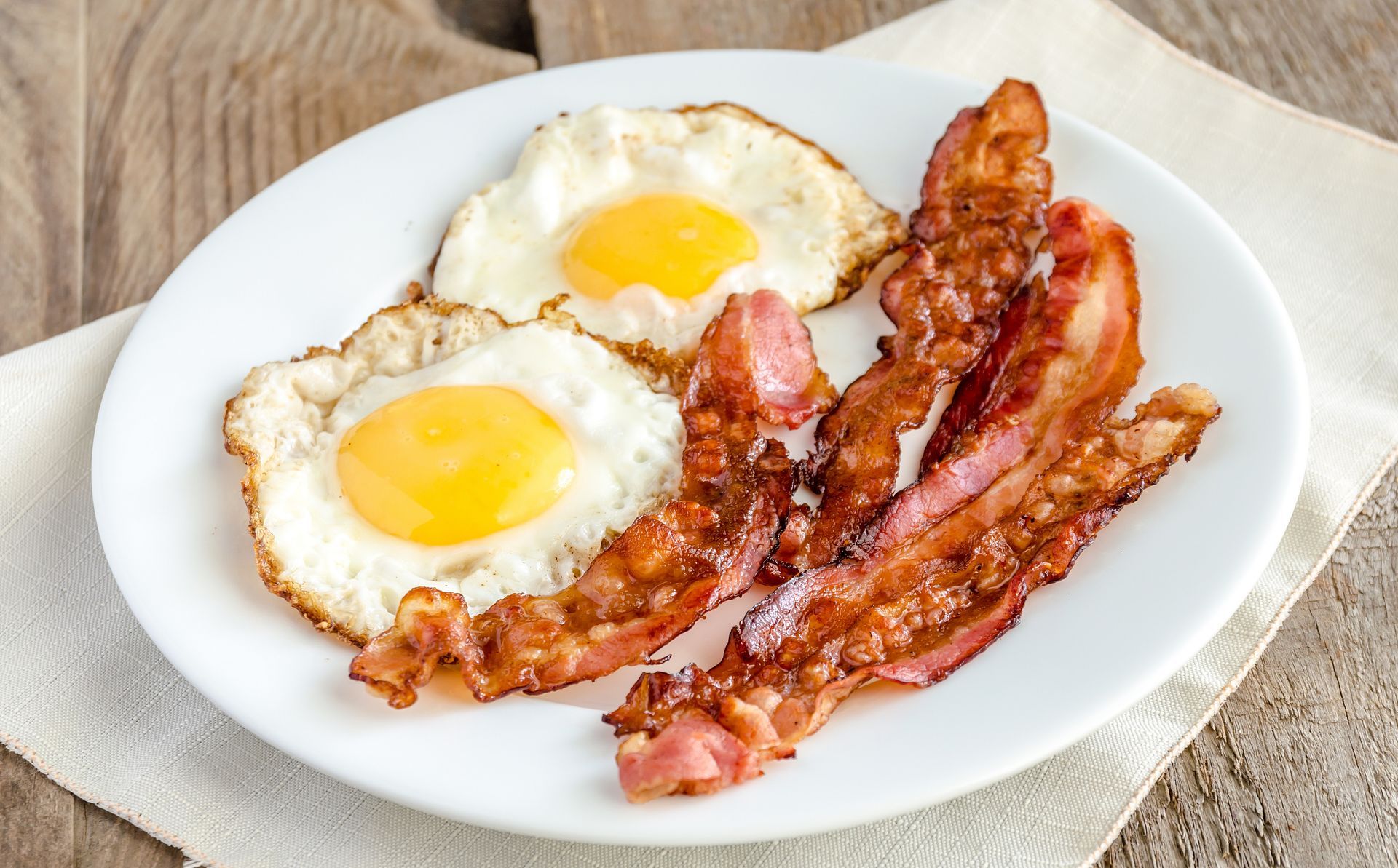 Two fried eggs with bright yellow yolks and strips of crispy bacon on a white plate.
