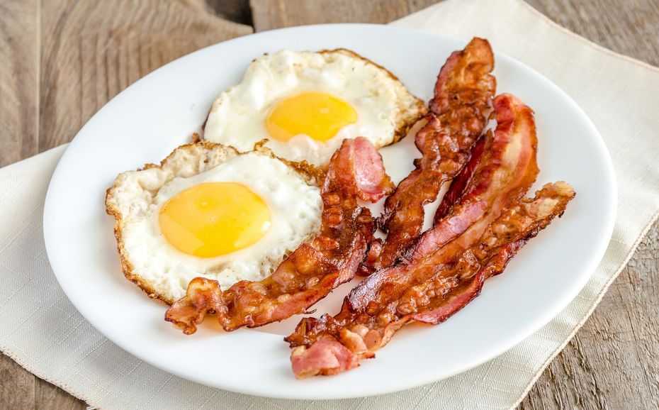 Two fried eggs with bright yellow yolks and strips of crispy bacon on a white plate.