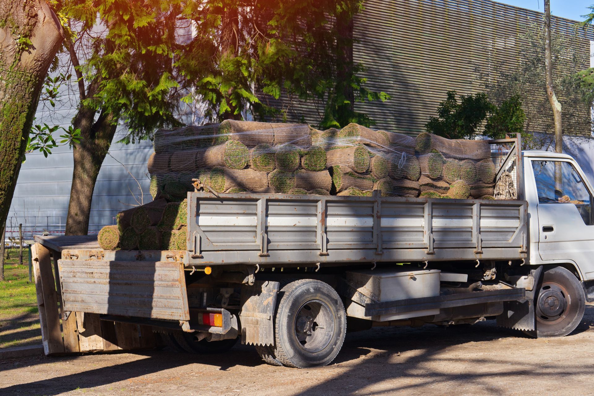Truck loaded with tree trunks parked beside a stone wall under trees