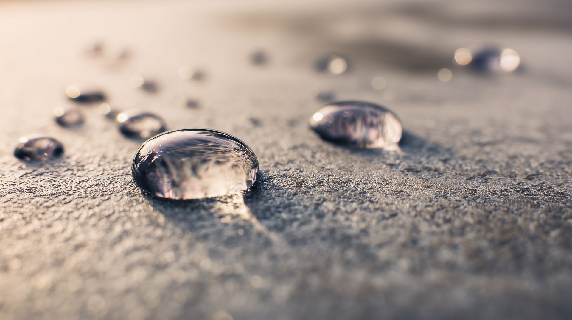 Macro close-up of water droplets on a textured surface with soft sunlight.