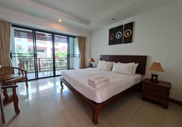 Bedroom with a bed, nightstand, lamps, and balcony access. Neutral tones, decorative wall art.