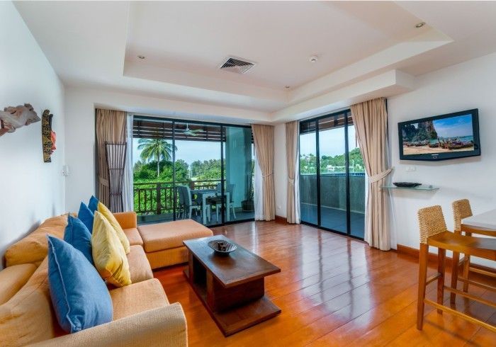 Bright living room with sectional sofa, balcony, hardwood floors, and TV.