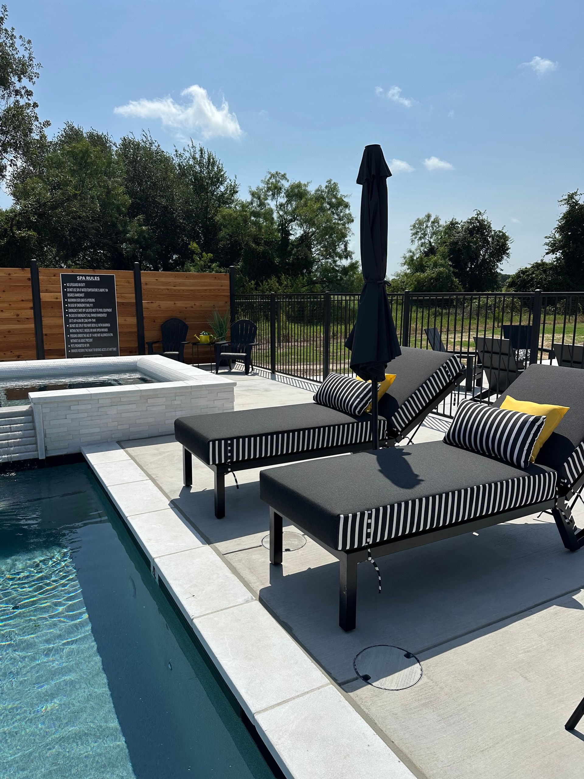 Poolside lounge chairs beside a blue swimming pool under a sunny sky.