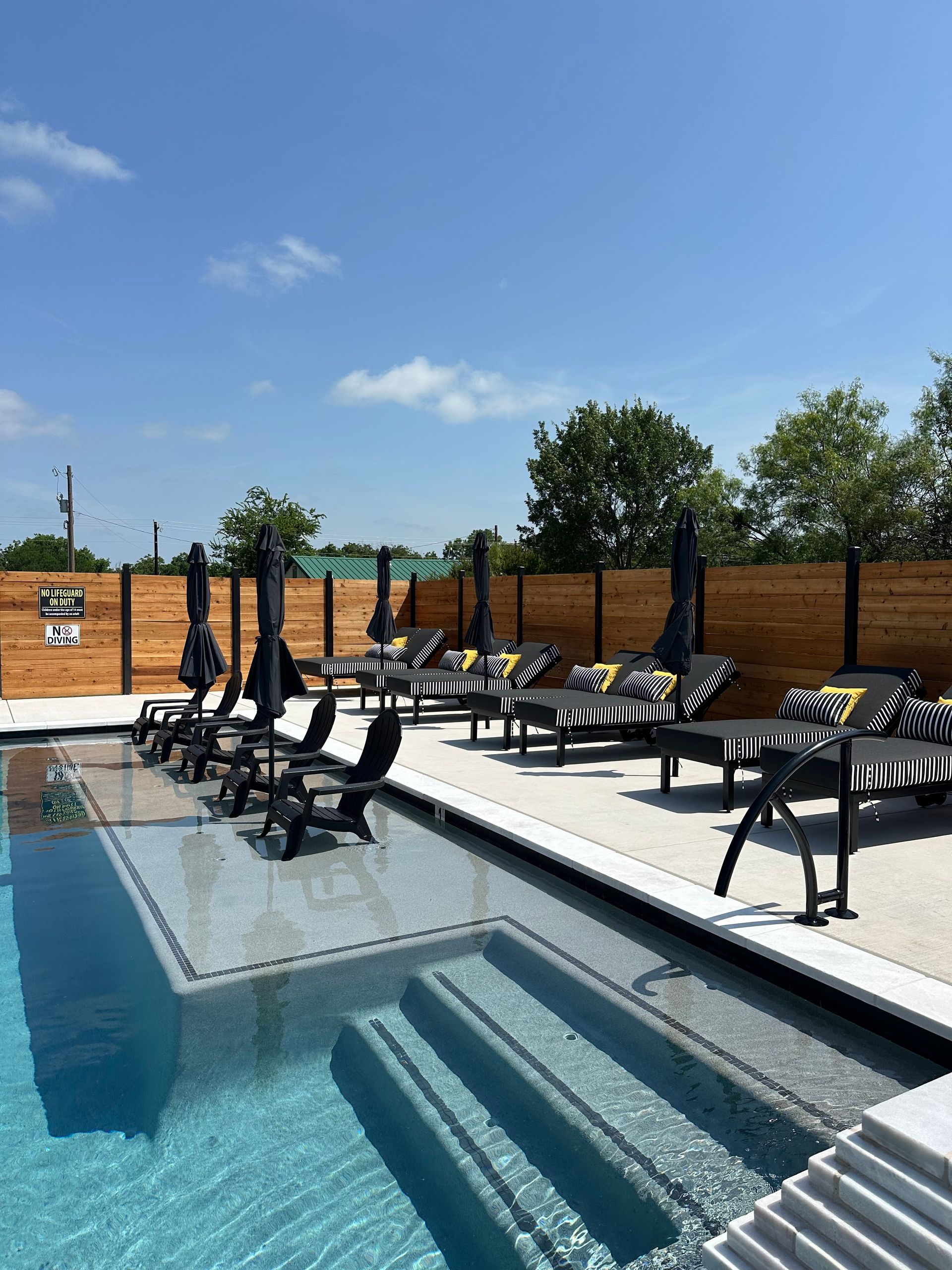 Backyard pool with lounge chairs and black umbrellas under a blue sky