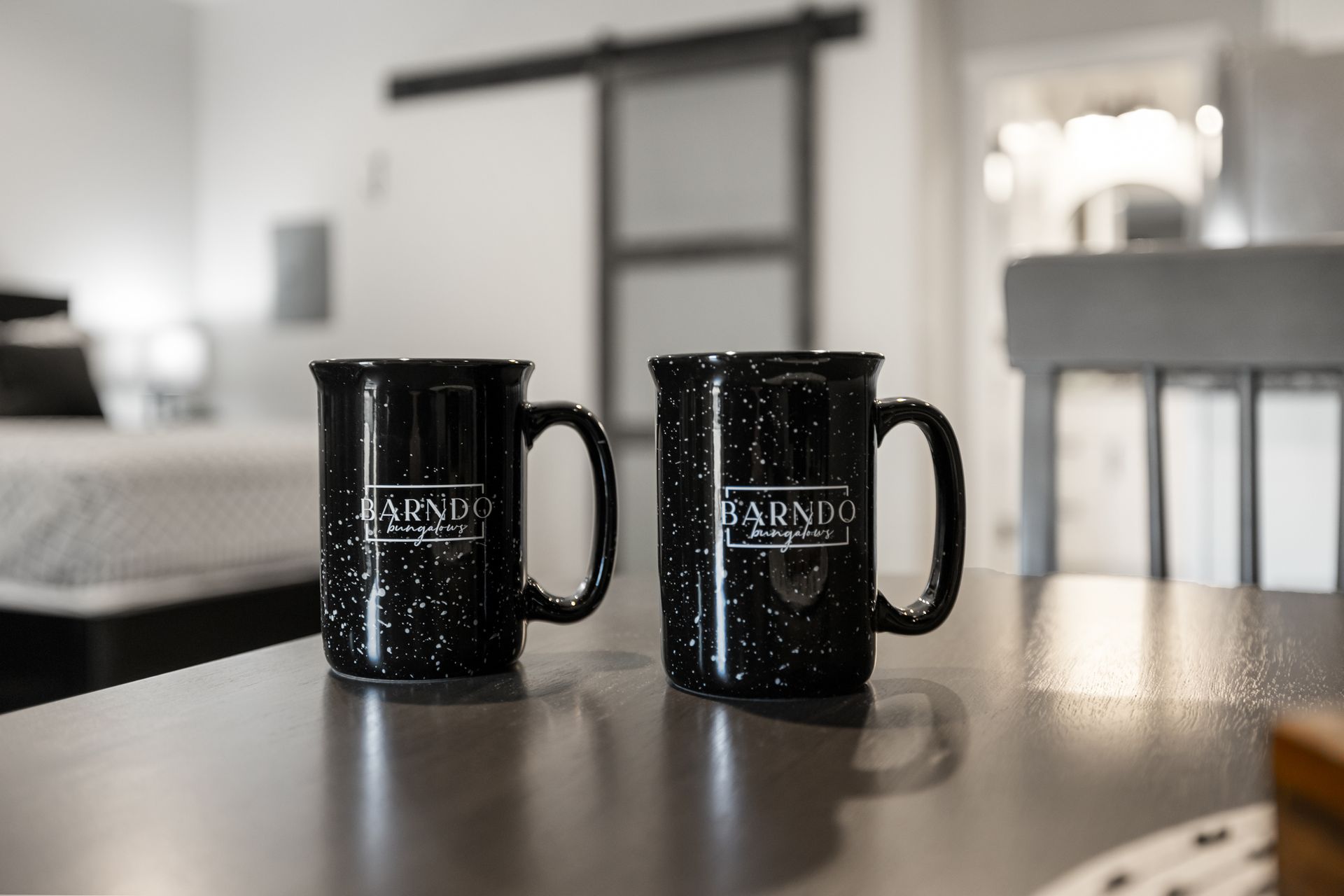 Two black speckled mugs on a table in a bright kitchen or dining room
