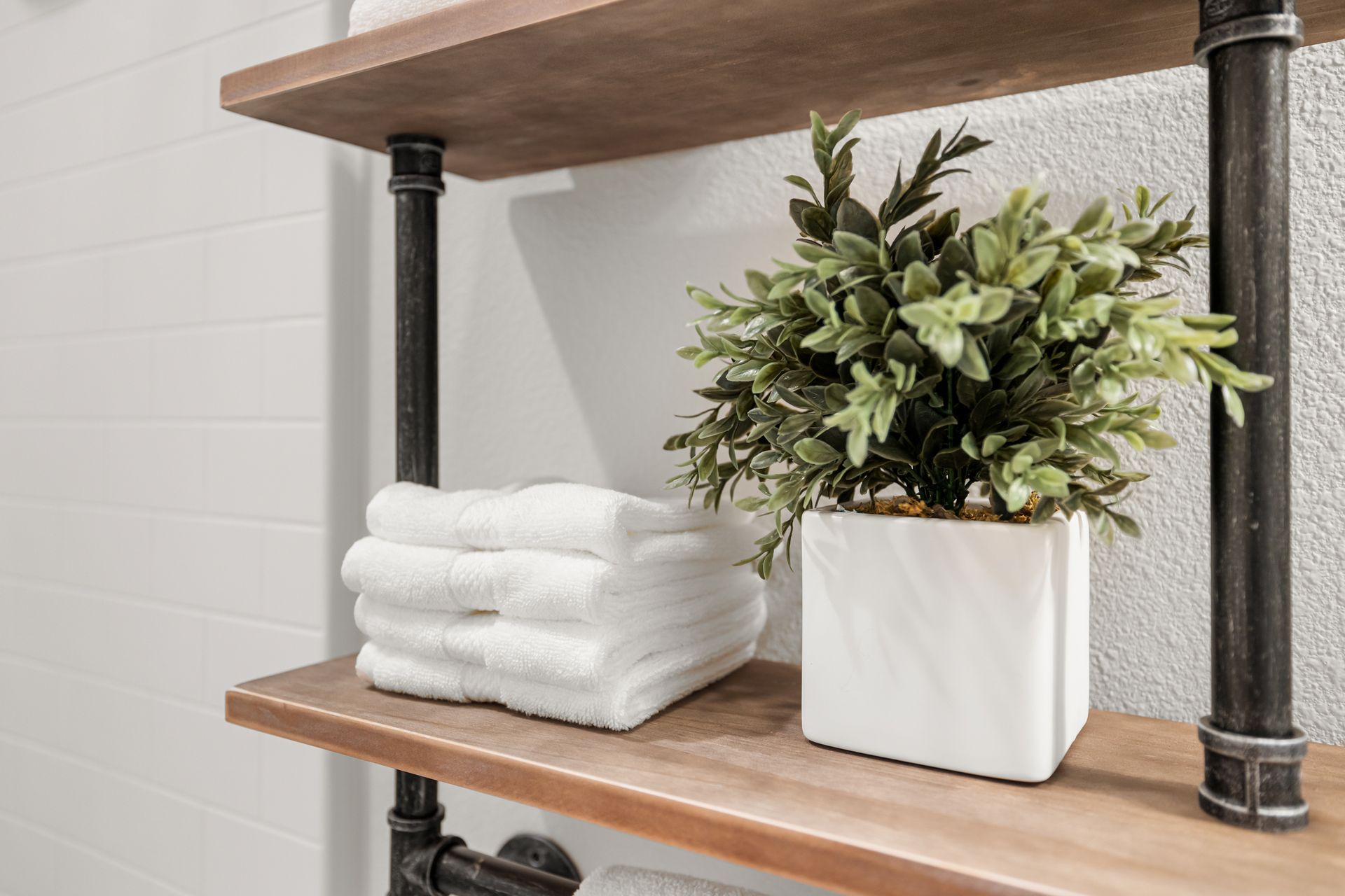 Wooden shelves with folded white towels and a potted green plant in a bathroom