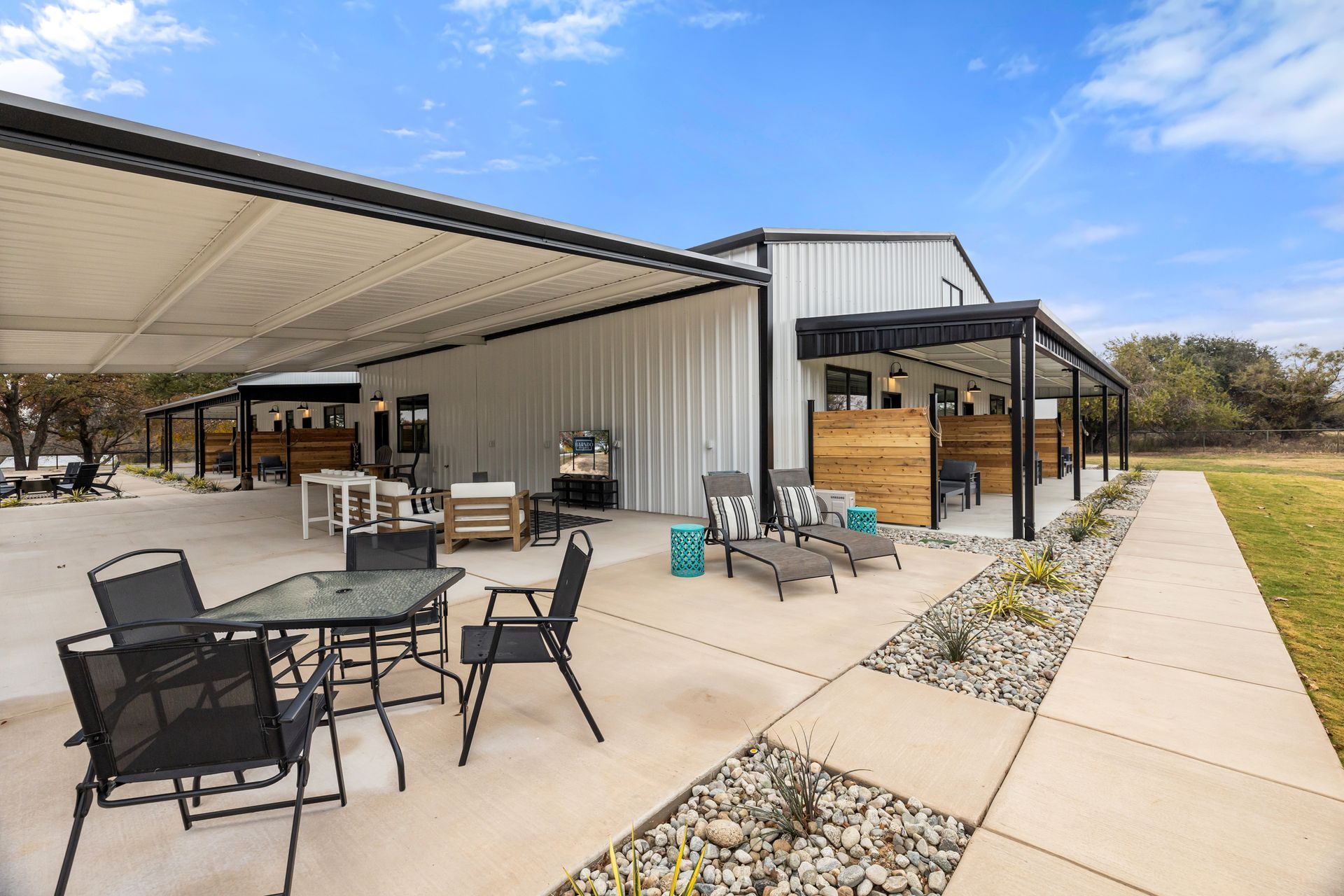 Patio with outdoor tables and chairs beside a modern metal building under a clear blue sky