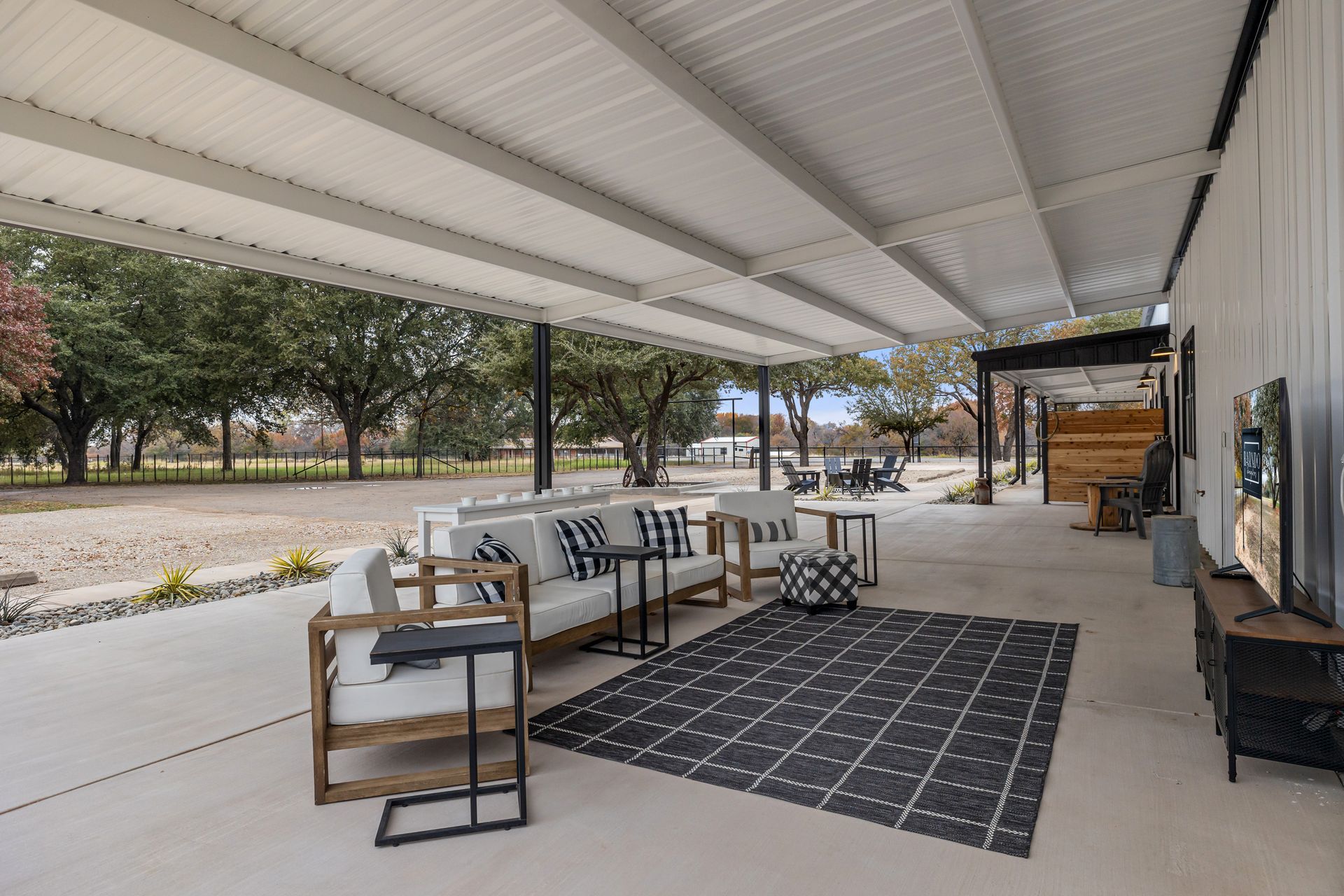 Covered patio seating area with chairs, table, and rug beside a white building and open yard