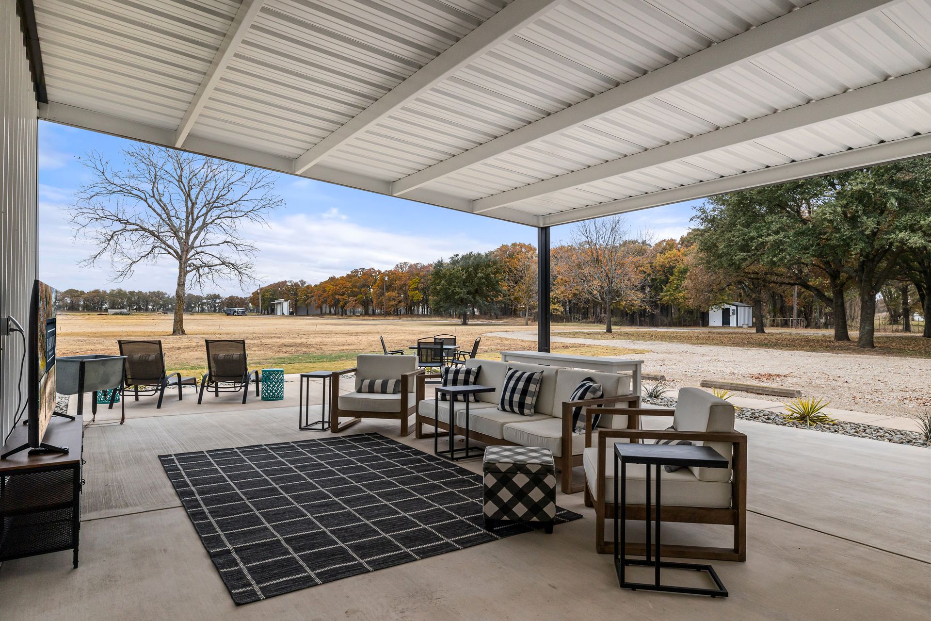 Covered patio with outdoor seating, striped rug, and open view of a grassy field under a cloudy sky