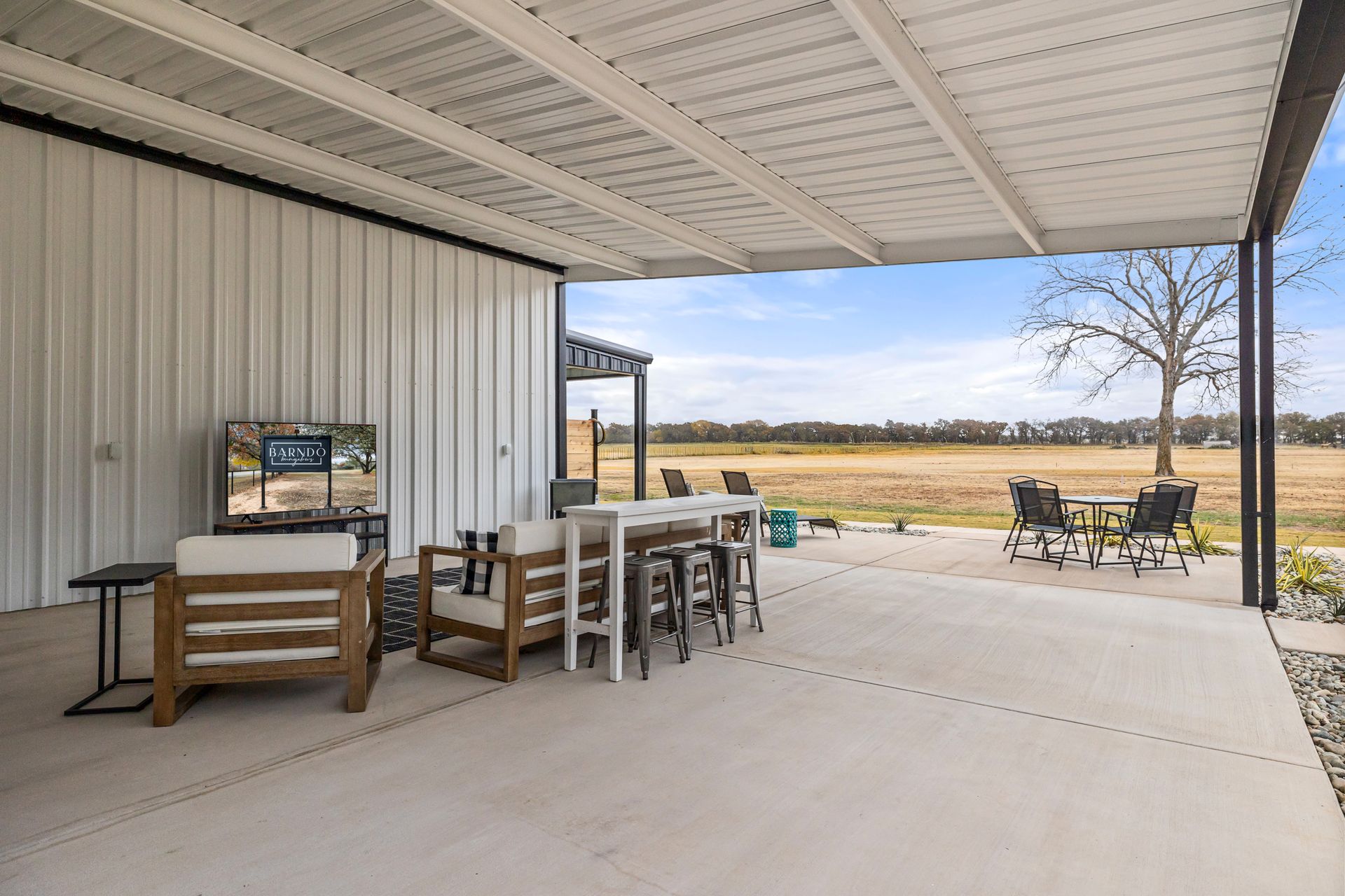 Covered patio with dining table and chairs overlooking a grassy yard and open fields