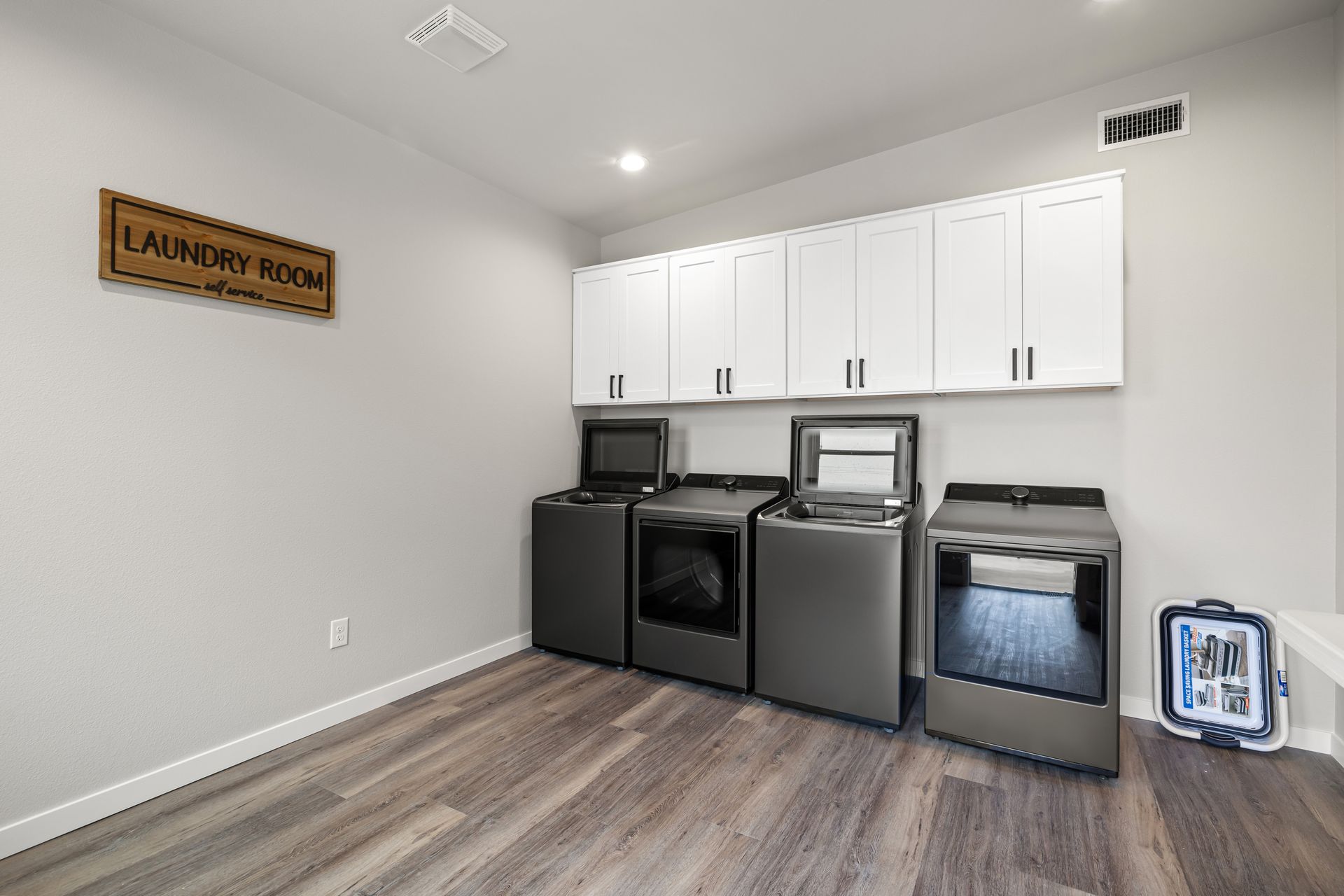Laundry room with white cabinets, gray washer and dryer, black mini fridge, and a wood sign on the wall
