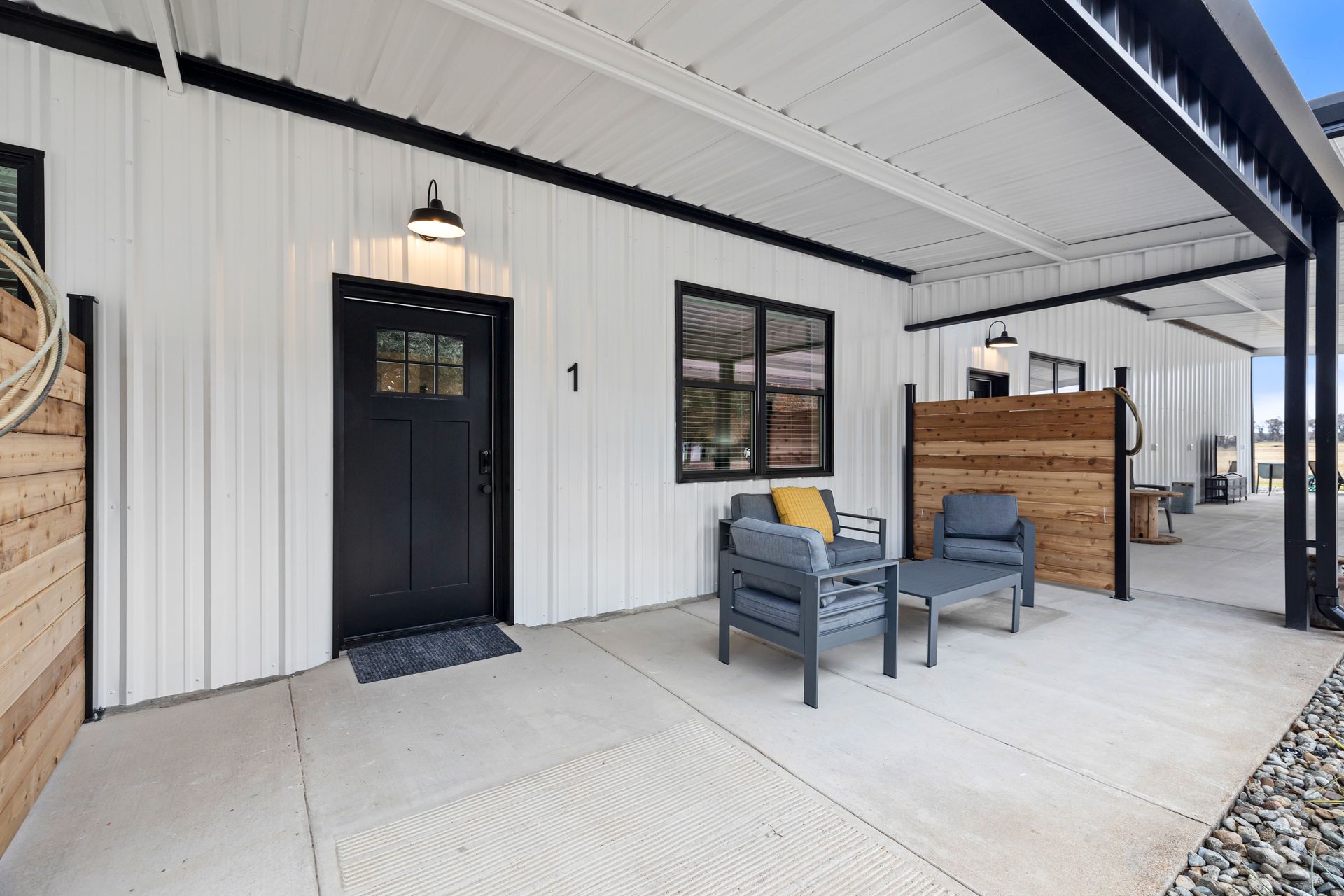 Modern house porch with black door, gray chairs, small table, and covered patio seating area
