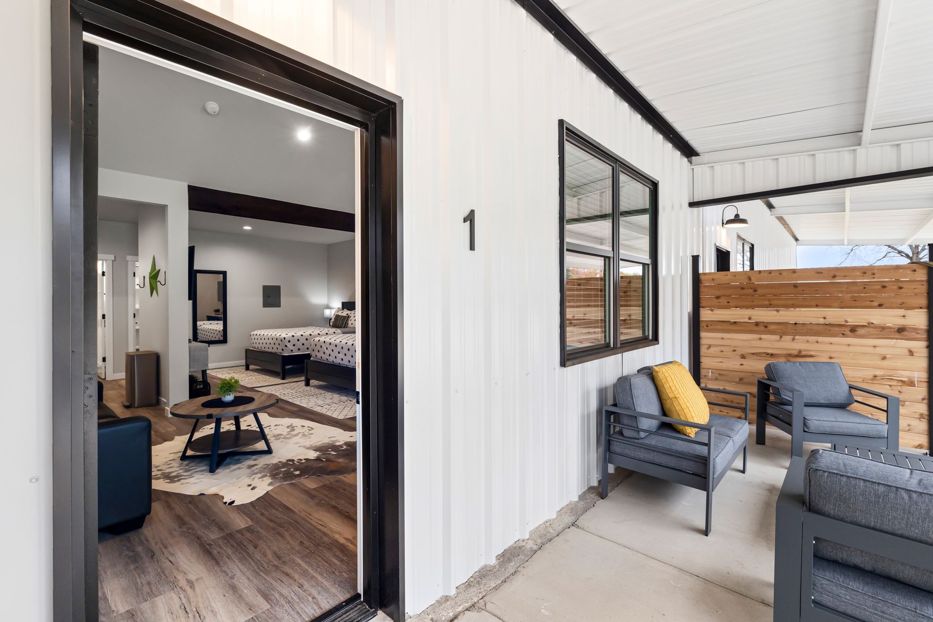 Modern porch with wicker chairs, yellow cushion, and open doorway into a bright living room.