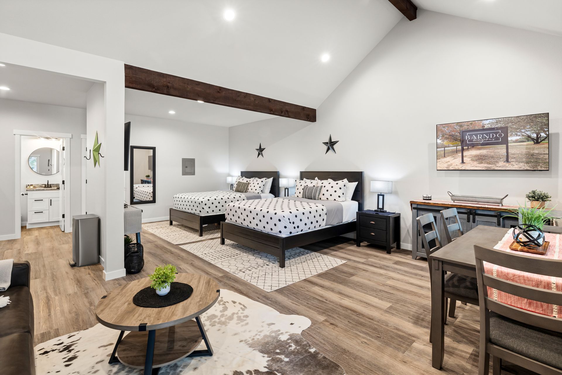 Modern bedroom with a patterned bed, wood beams, white walls, and a small sitting area.
