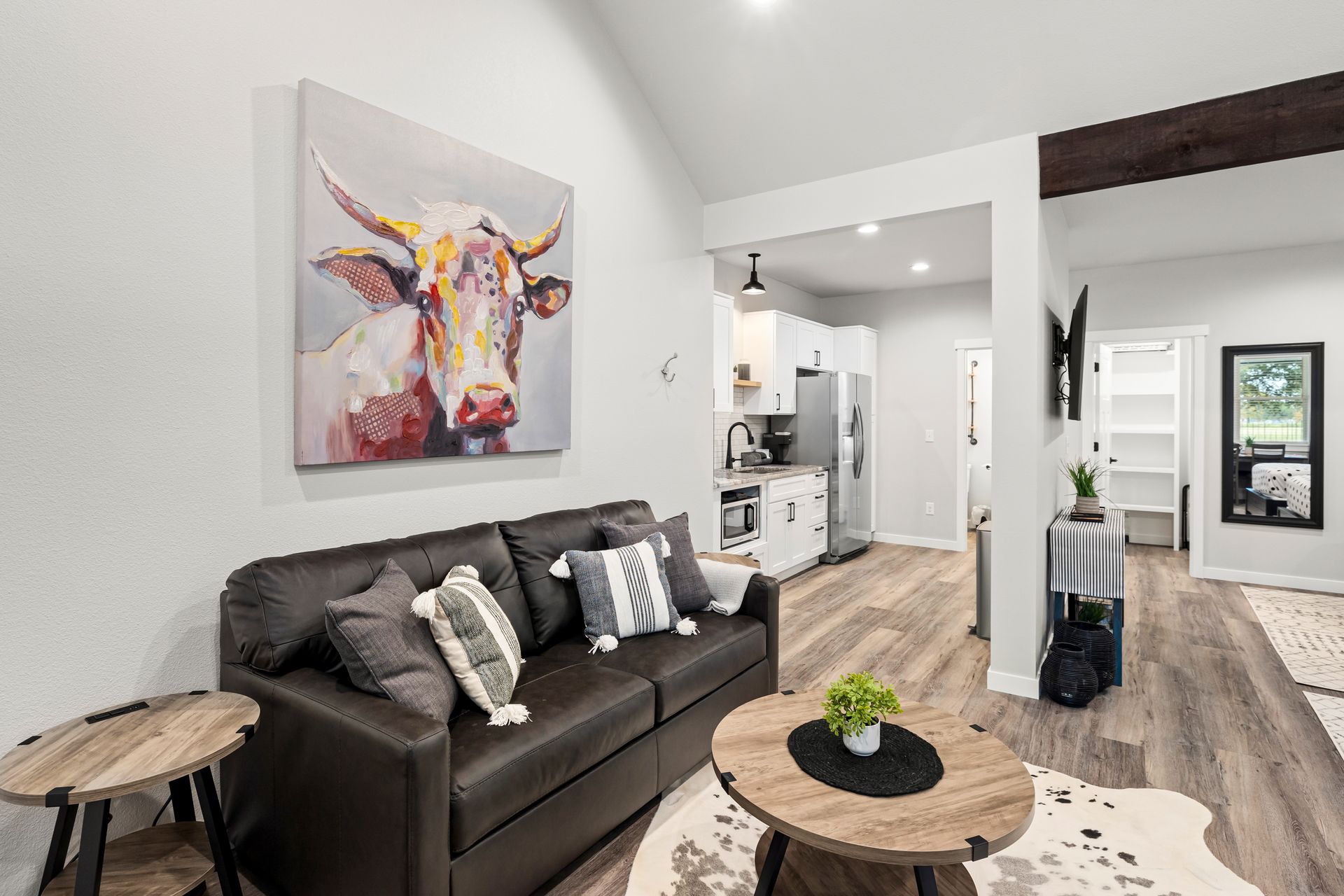 Modern living room with dark sofa, round wooden tables, abstract wall art, and open kitchen view