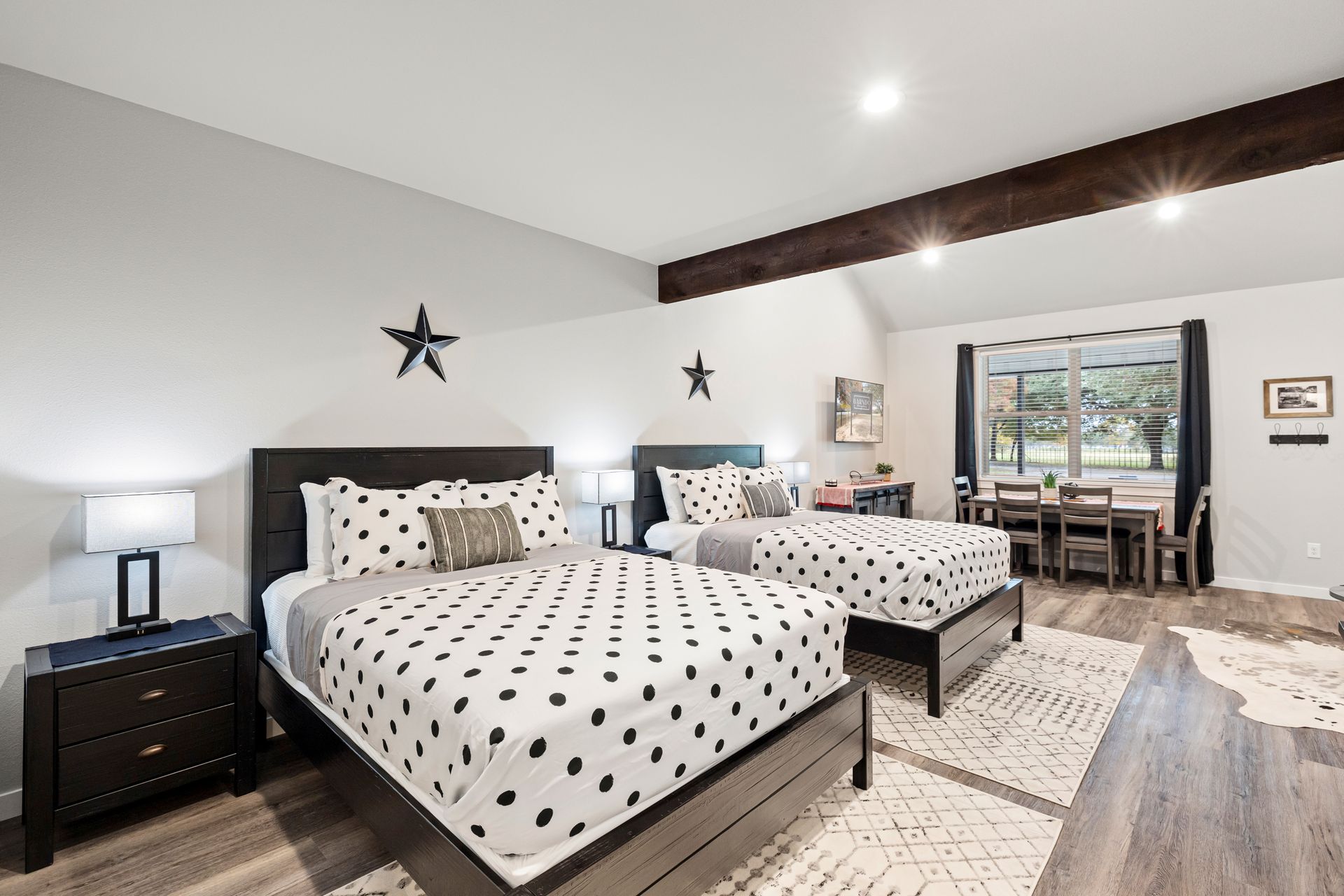 Spacious bedroom with two white polka-dot beds, dark wood furniture, and a desk near a window view
