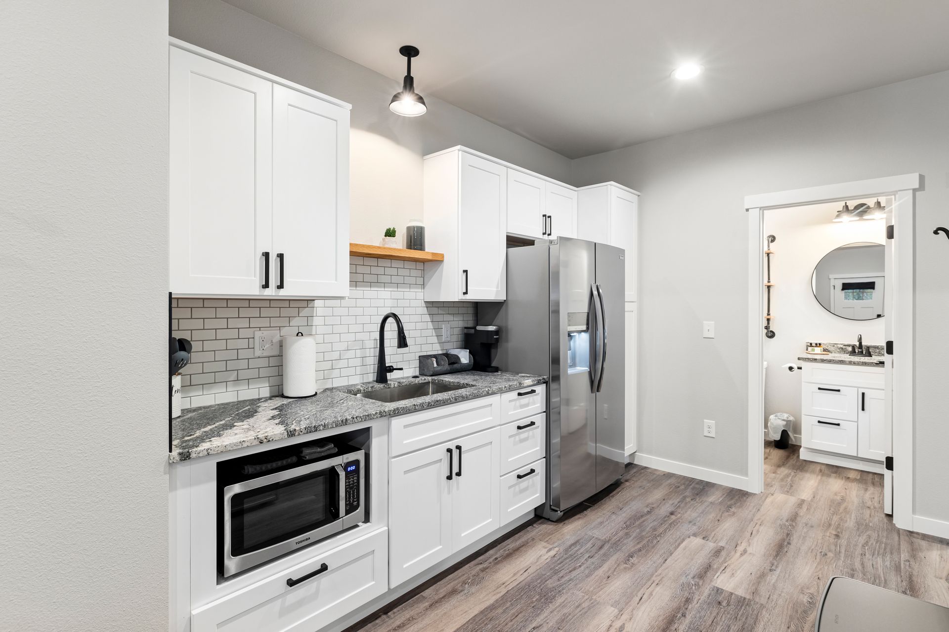 Modern white kitchen with stainless steel appliances, gray backsplash, and light wood flooring.