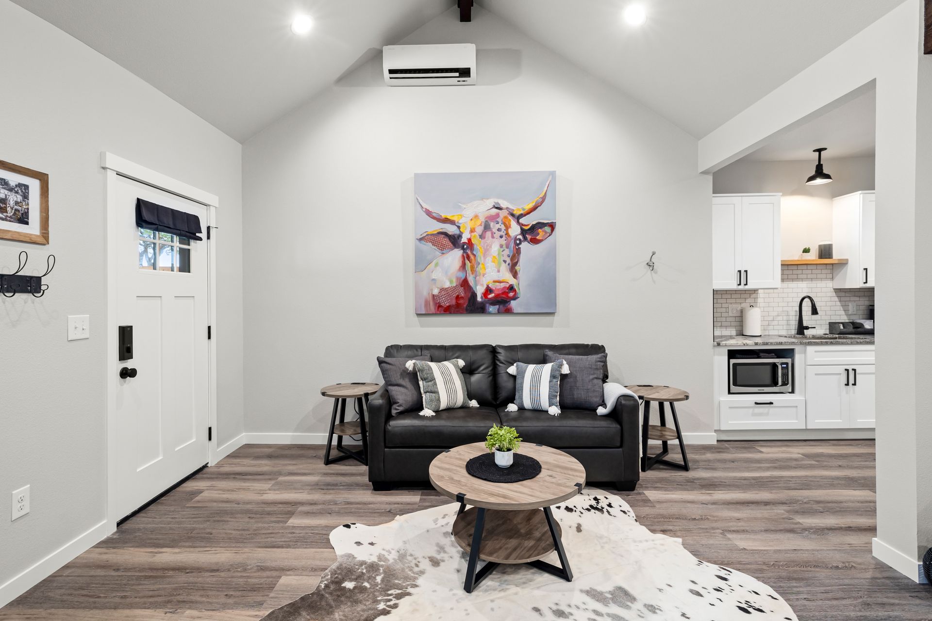 Modern living room with black sofa, cow artwork, round coffee table, and open kitchen view