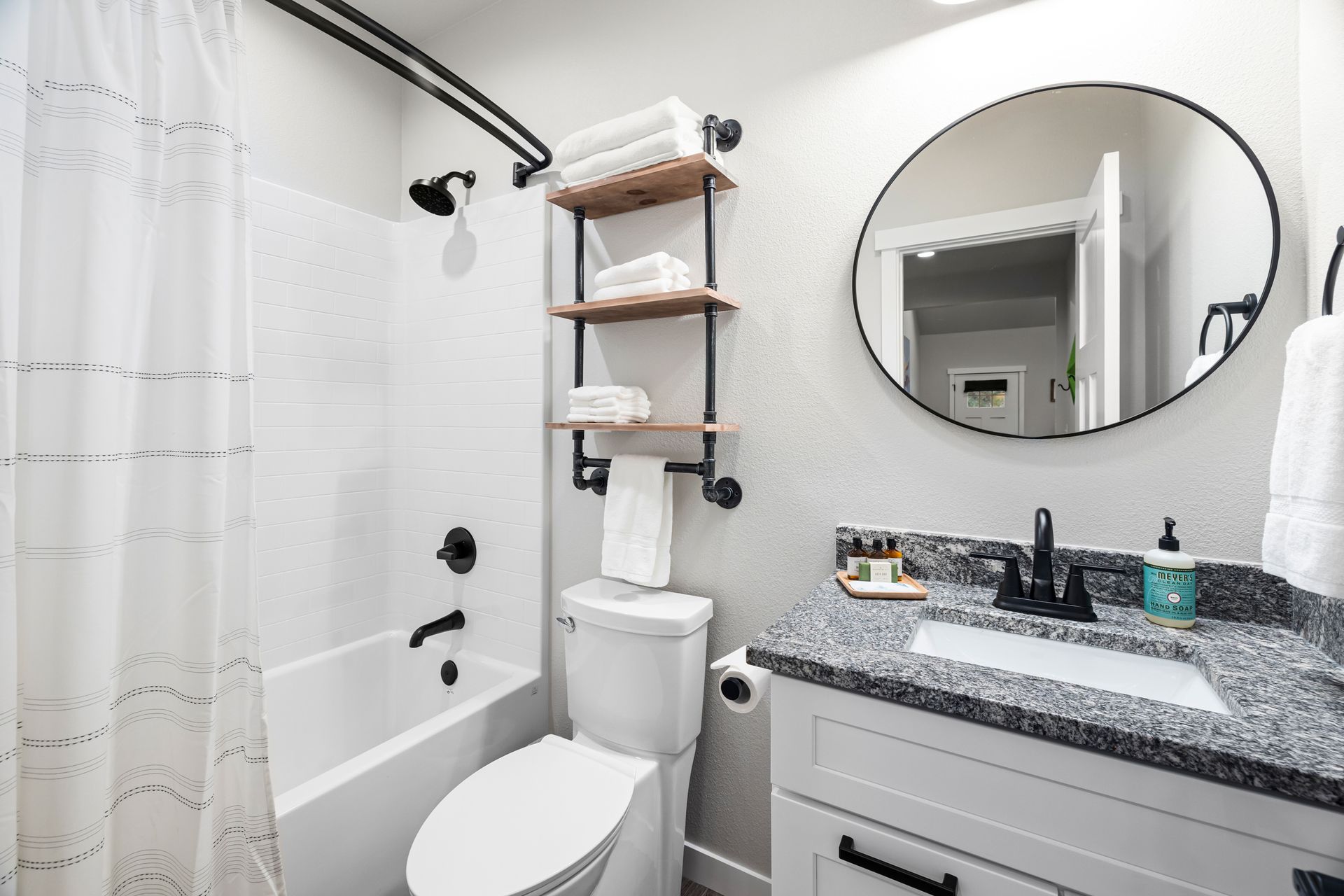 Bright white bathroom with shower curtain, toilet, vanity, and round mirror