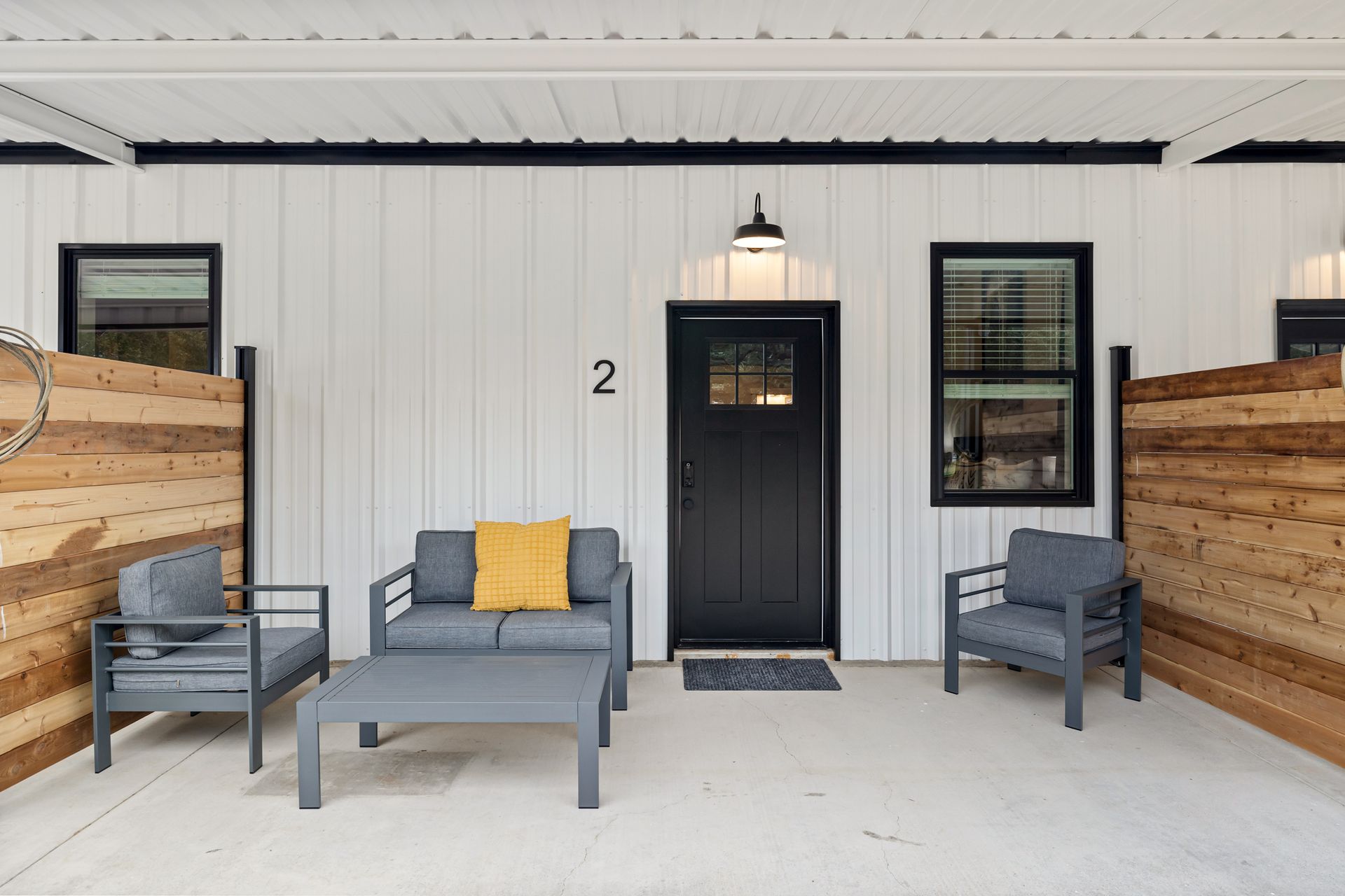 Porch with black door, gray seating, and wood planters against white siding