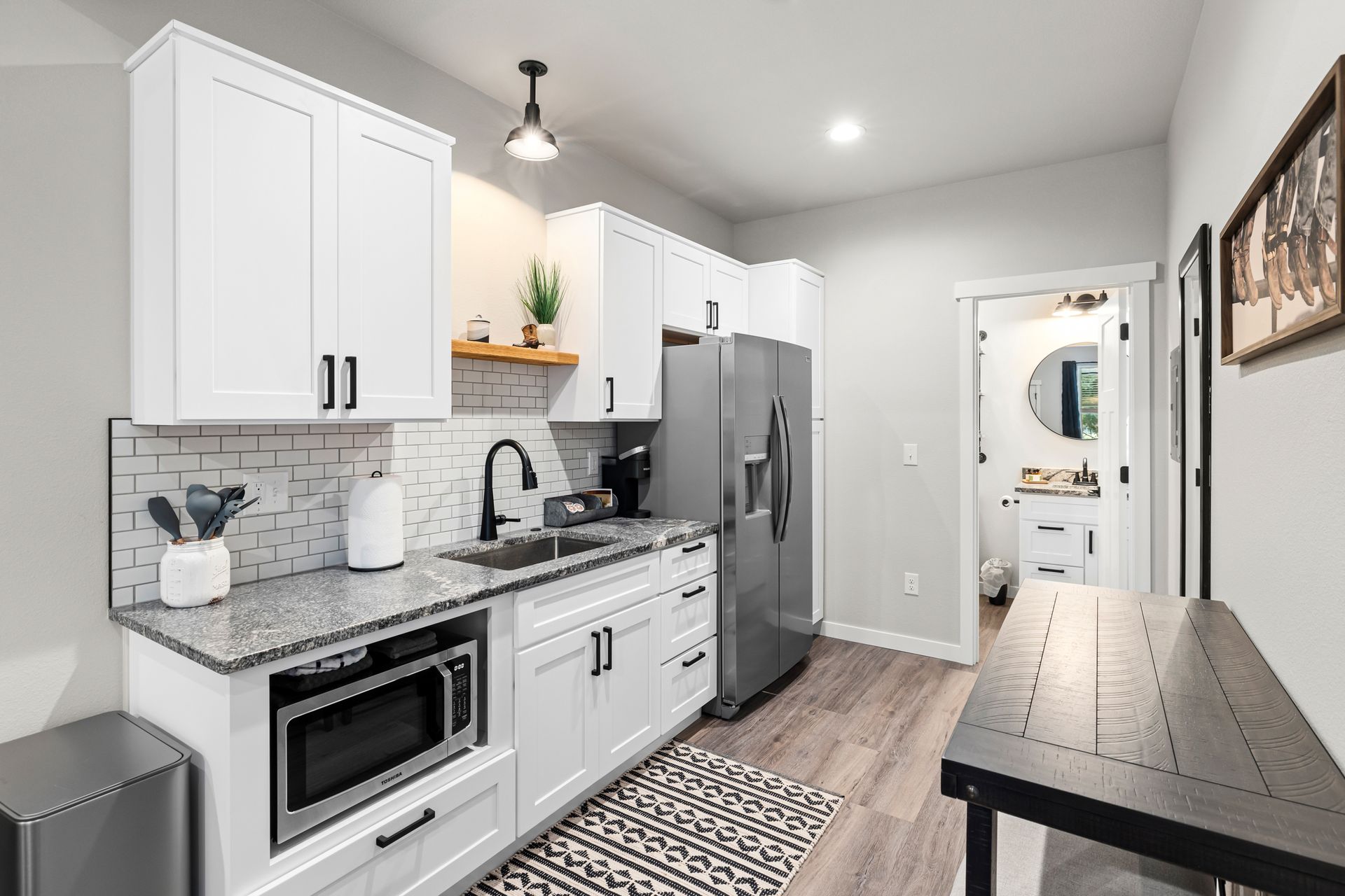 Modern white kitchen with stainless appliances, gray backsplash, and a small black table by the hallway