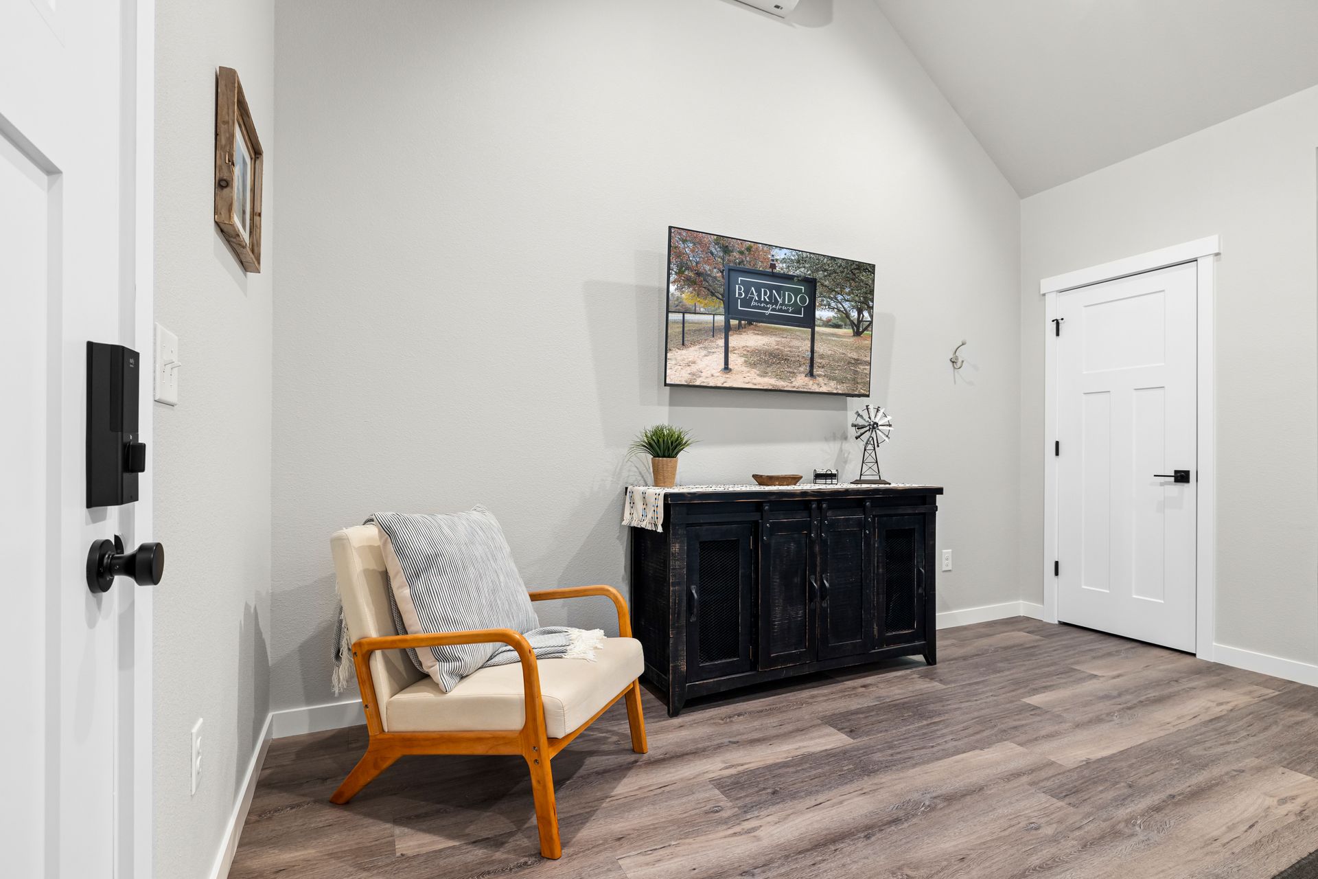 Minimalist room with a black cabinet, wooden chair, wall art, and a white door on light wood floors.