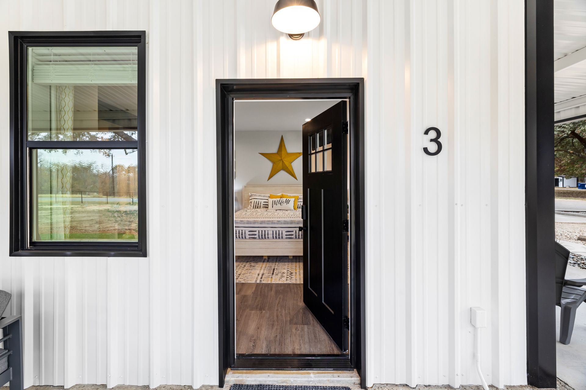 Small white building entrance with black trim, open door, gold star inside, and number 3 beside it.