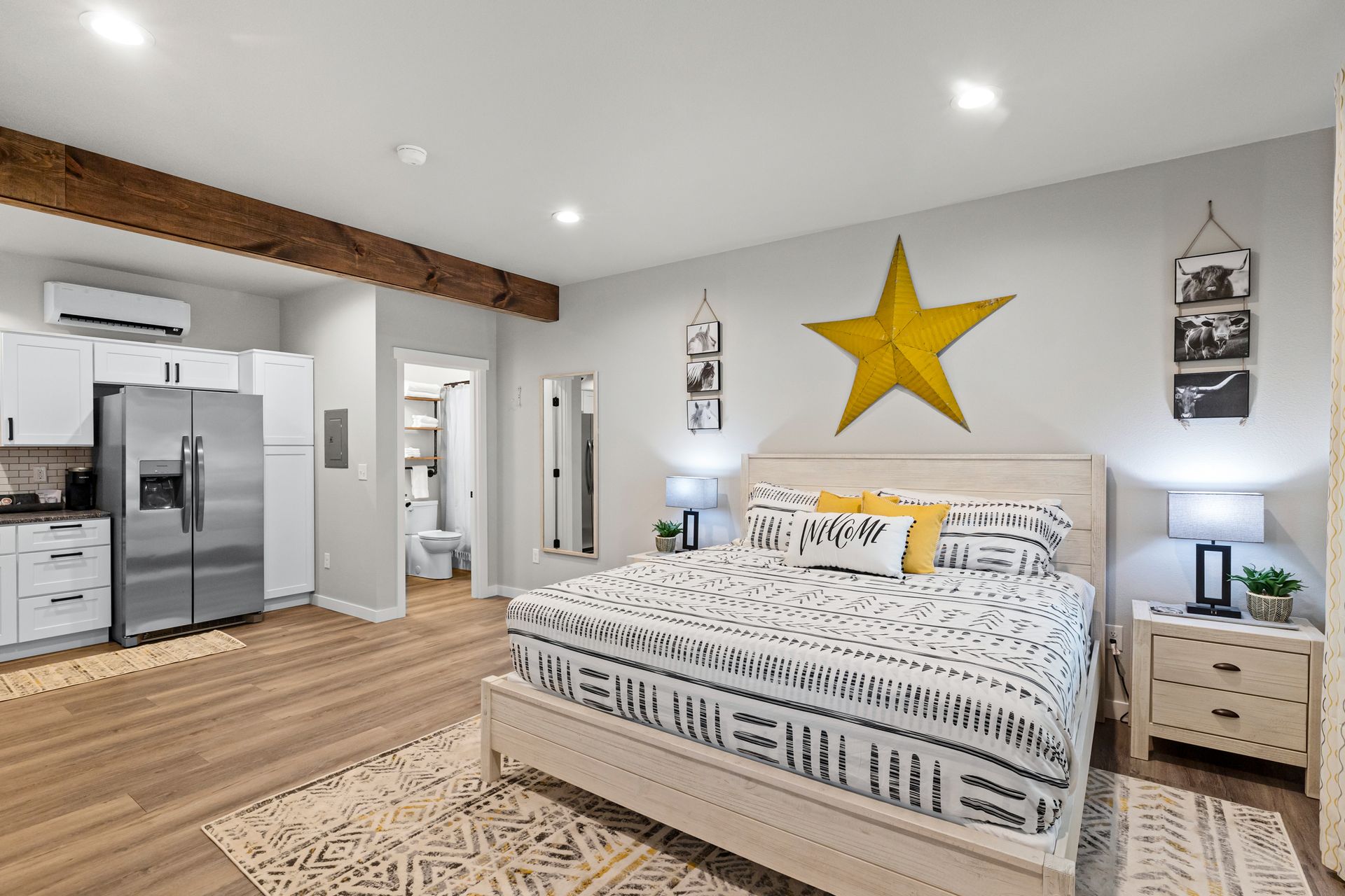 Bright bedroom with a king bed, yellow star wall art, nightstands, and open view into a modern kitchen