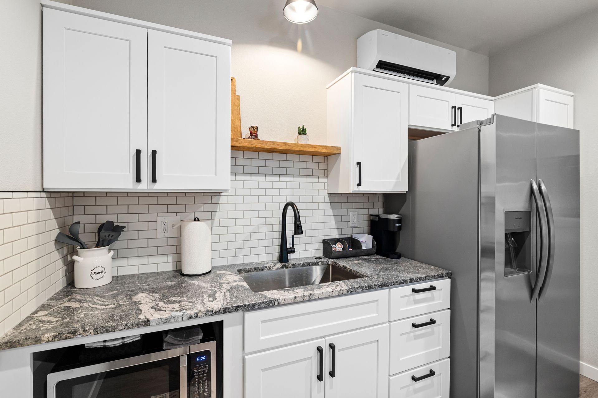 Modern white kitchen with granite counters, stainless steel appliances, and a black faucet