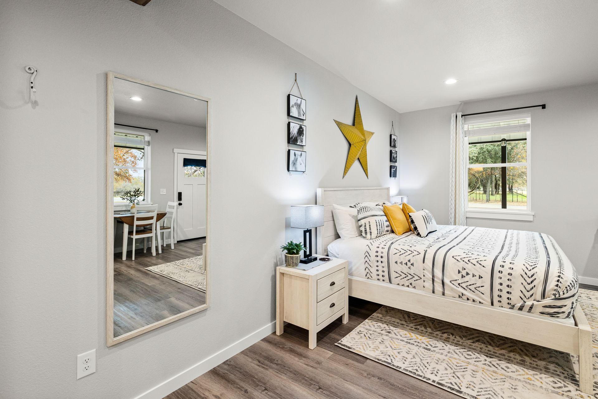 Bright bedroom with white bedding, star wall art, and a mirror reflecting a dining area.