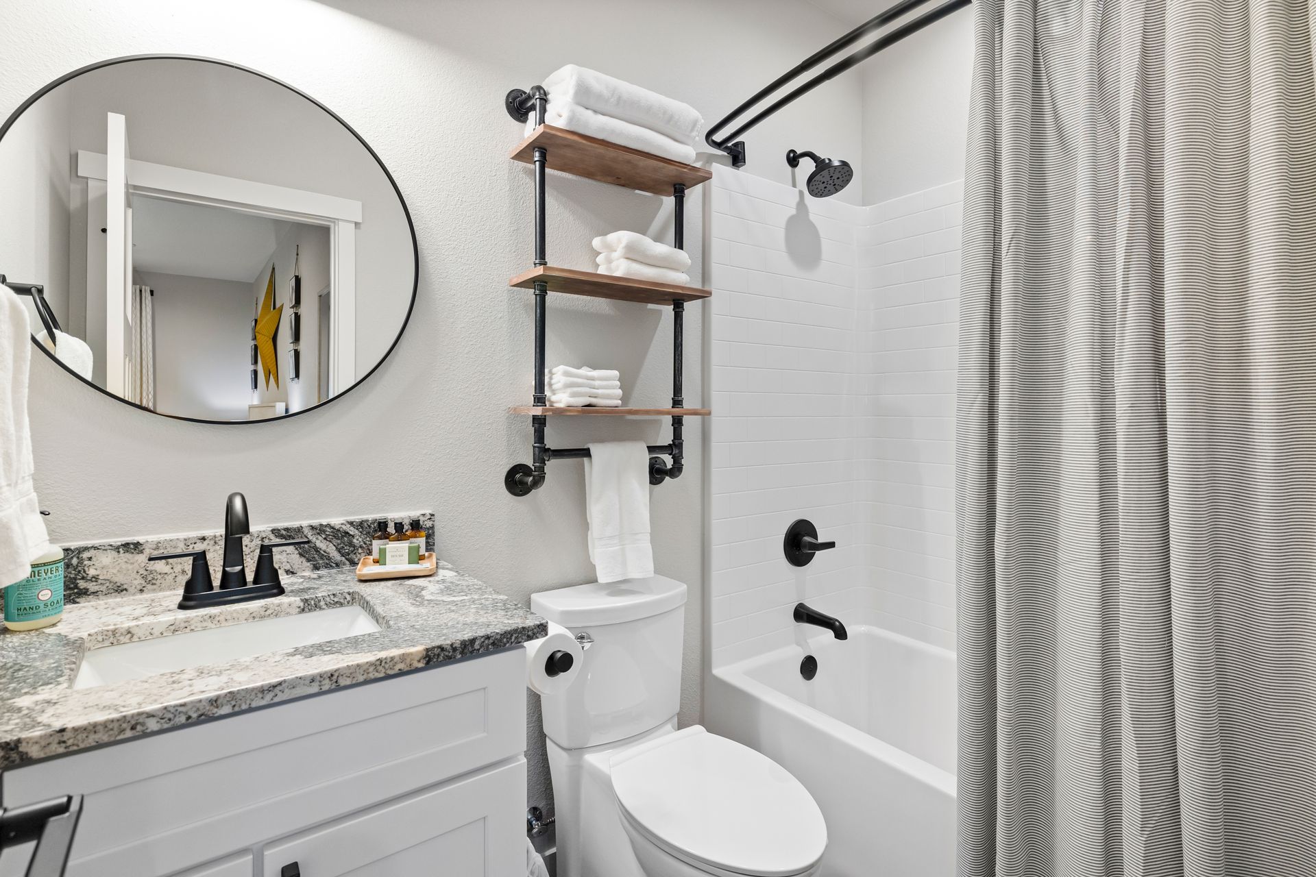 Modern bathroom with white vanity, round mirror, toilet, shower, and patterned curtain