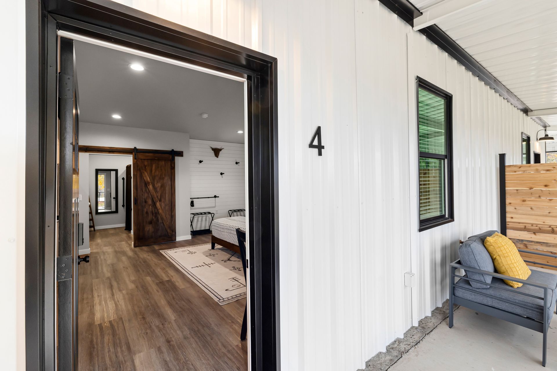 Front porch entrance to a white tiny house with black trim, number 4, and a glimpse of the interior inside