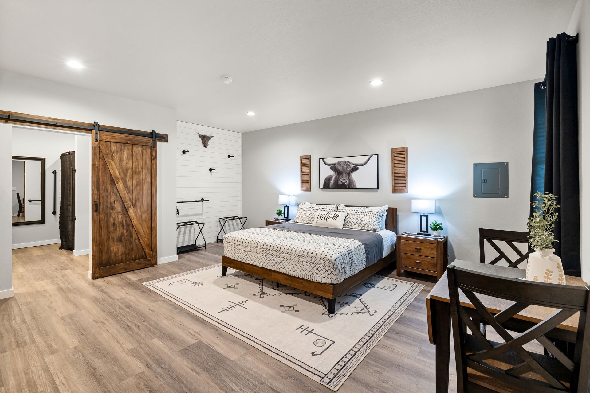 Spacious bedroom with a bed, wood sliding barn door, desk, rug, and wall art in neutral tones