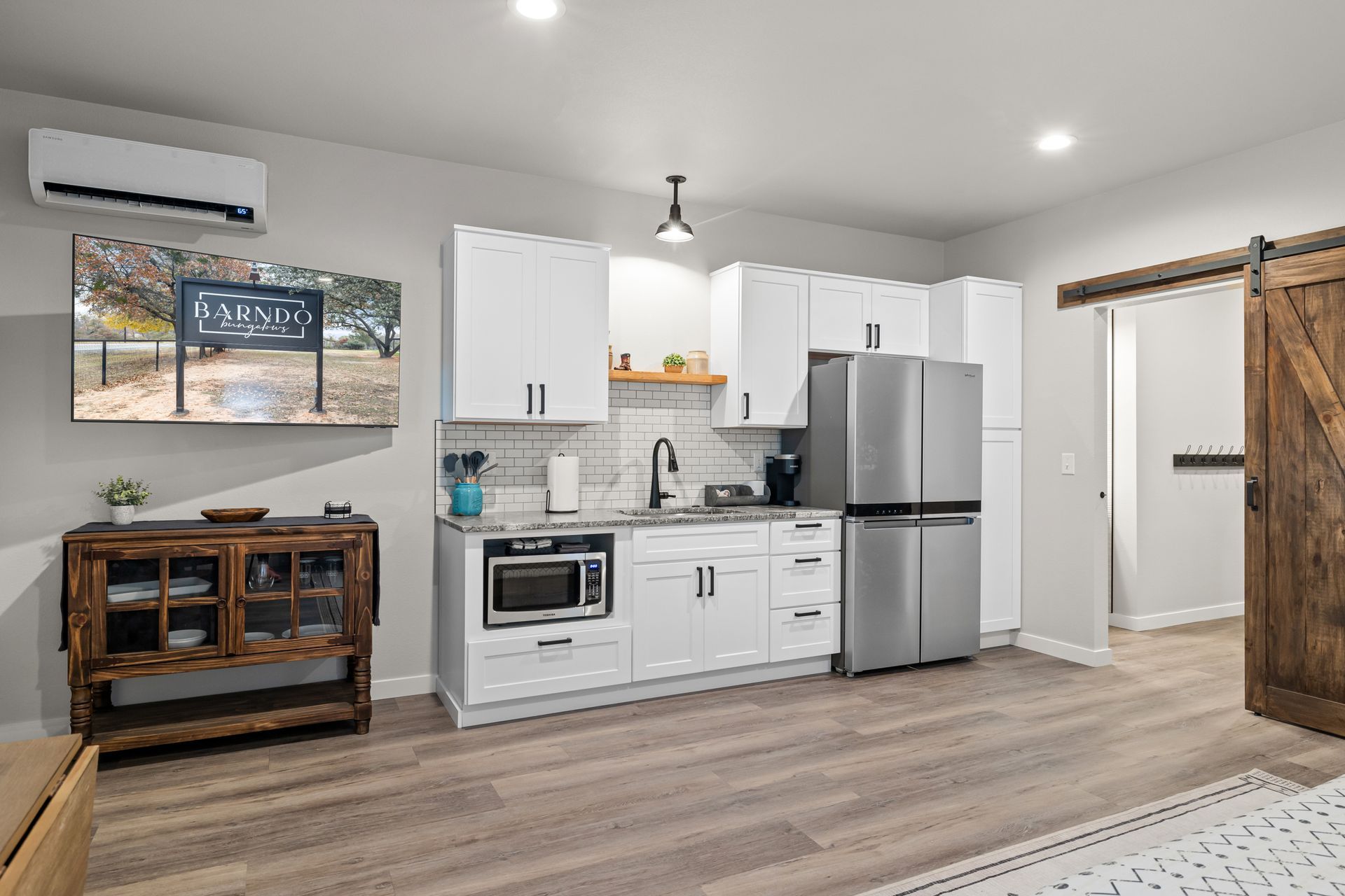 Modern white kitchen with stainless steel appliances, wood flooring, and a rustic console table