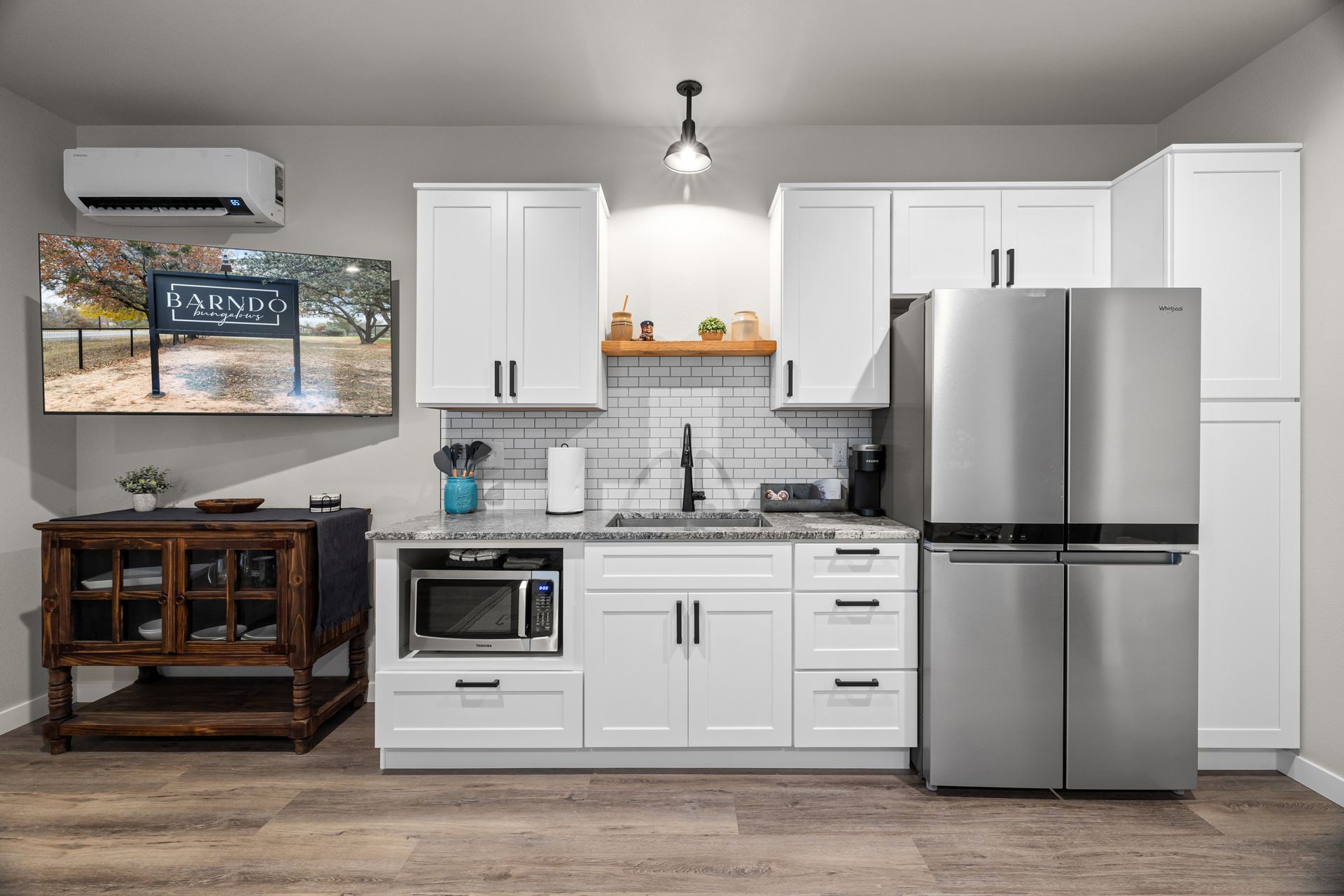 Modern kitchen with white cabinets, stainless steel fridge, stove, microwave, and wood sideboard.