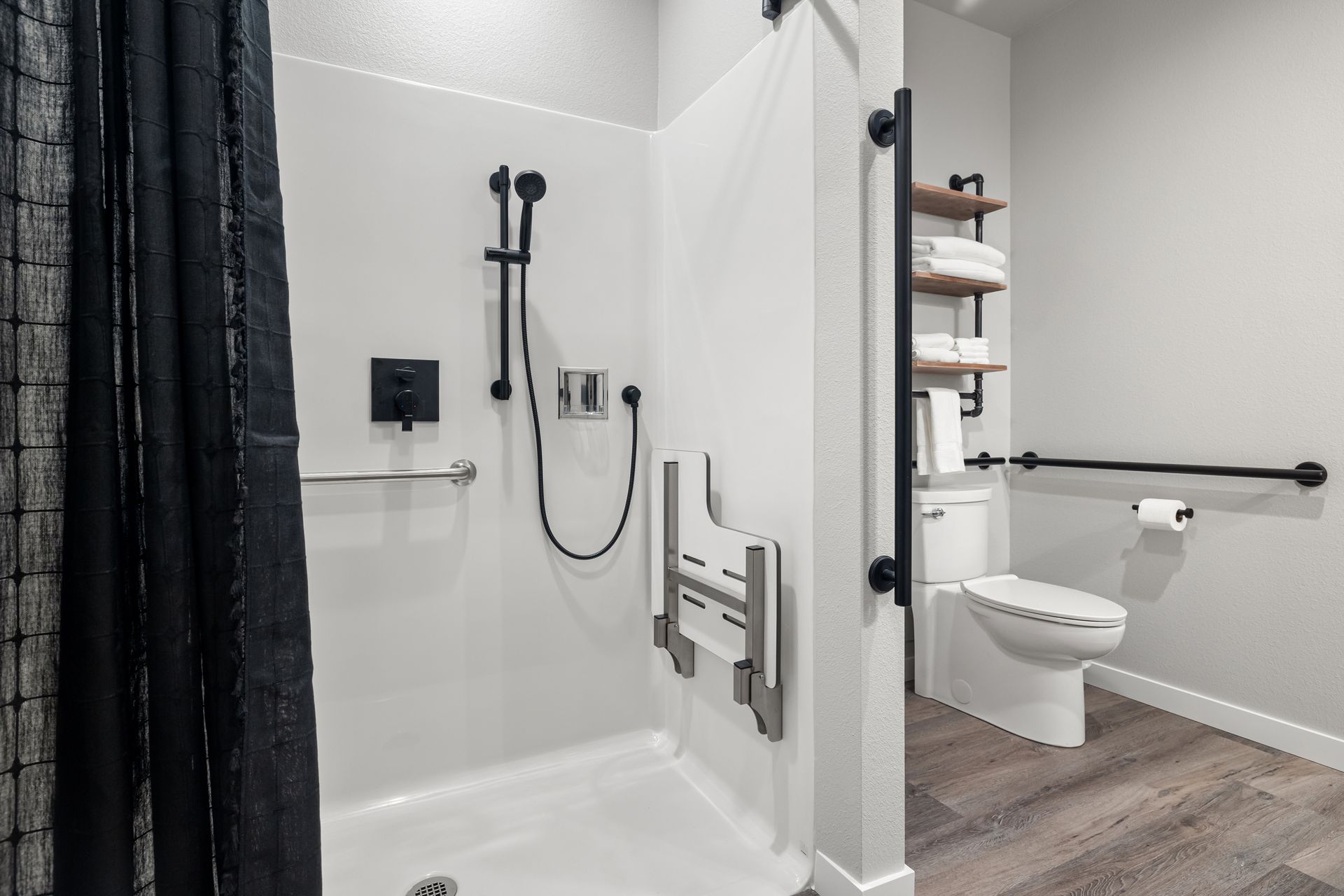 Accessible bathroom with walk-in shower, grab bars, shower seat, and toilet beside open shelving.
