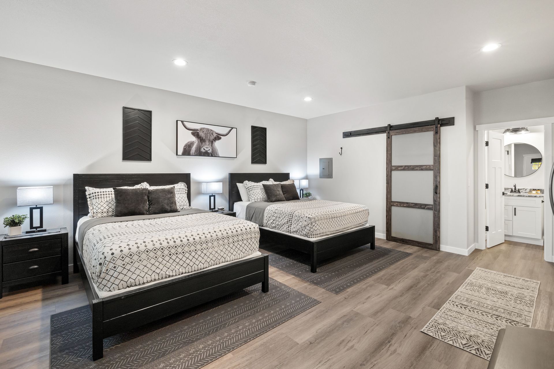 Modern bedroom with two beds, dark wood flooring, sliding barn door, and an adjoining bathroom