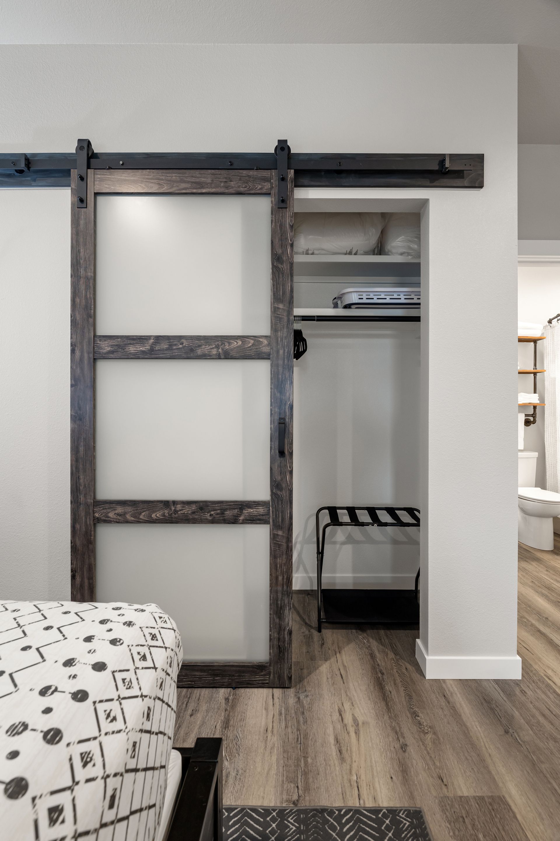 Rustic sliding barn door in a bedroom, partially open to a closet with shelves and a black stool.