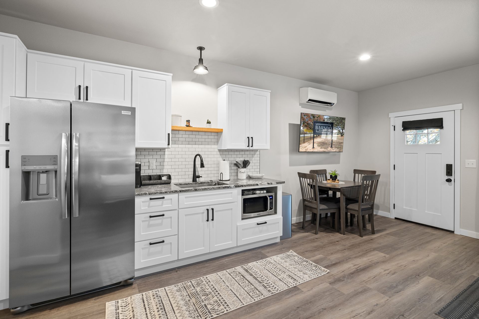 Bright modern kitchen and dining area with stainless steel appliances, white cabinets, and a small table by the window
