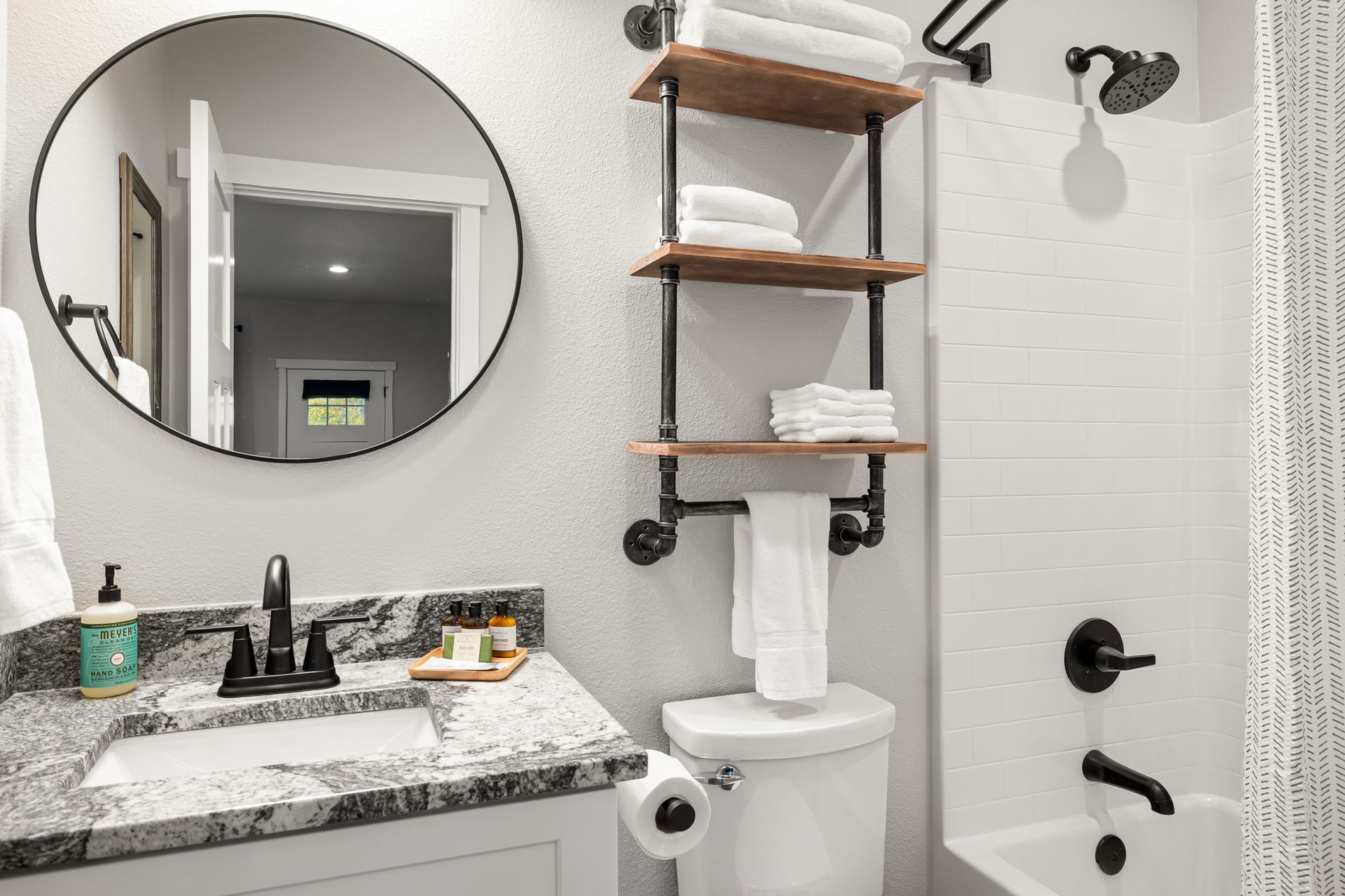 Modern bathroom with round mirror, marble vanity, shelving, and walk-in shower