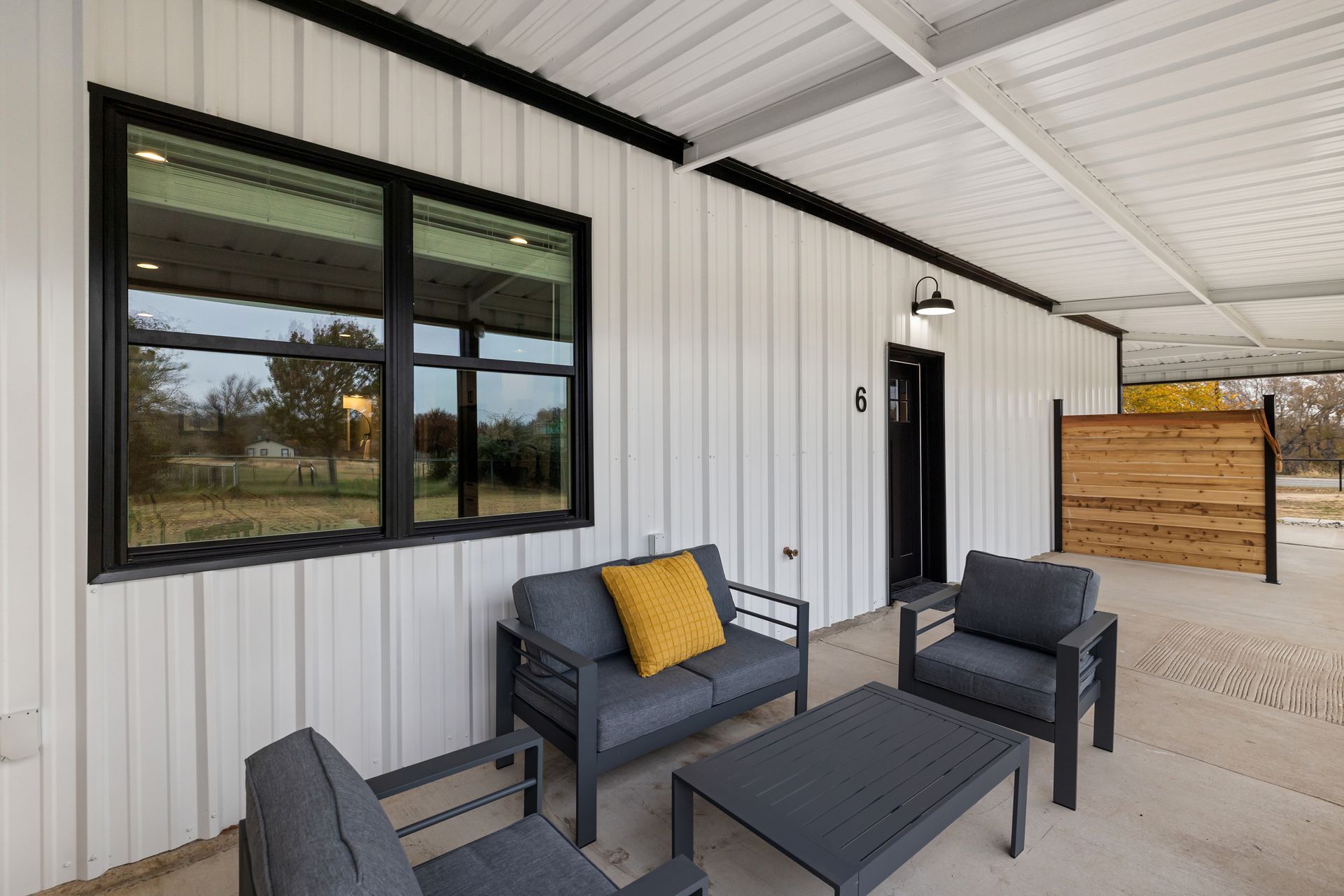 Covered porch with black chairs, small table, and black-framed window on a white exterior wall