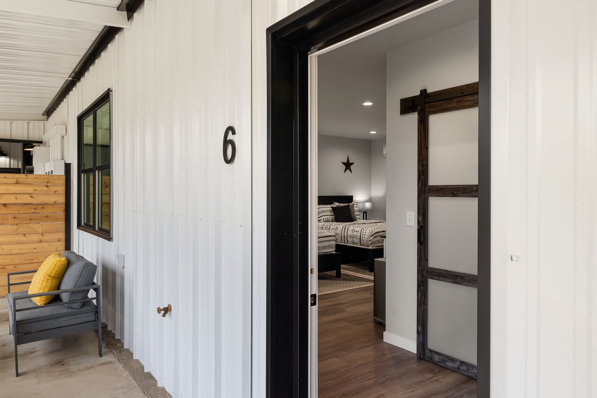 Open white doorway to house number 6 with black trim and a yellow cushion on a porch chair