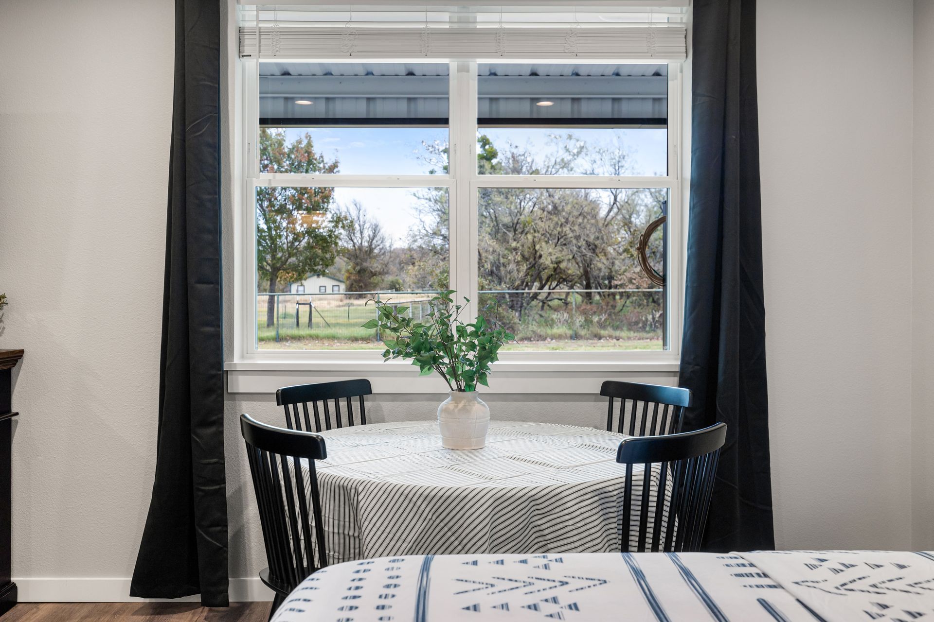 Dining area with black chairs, round table, and large window overlooking a yard.