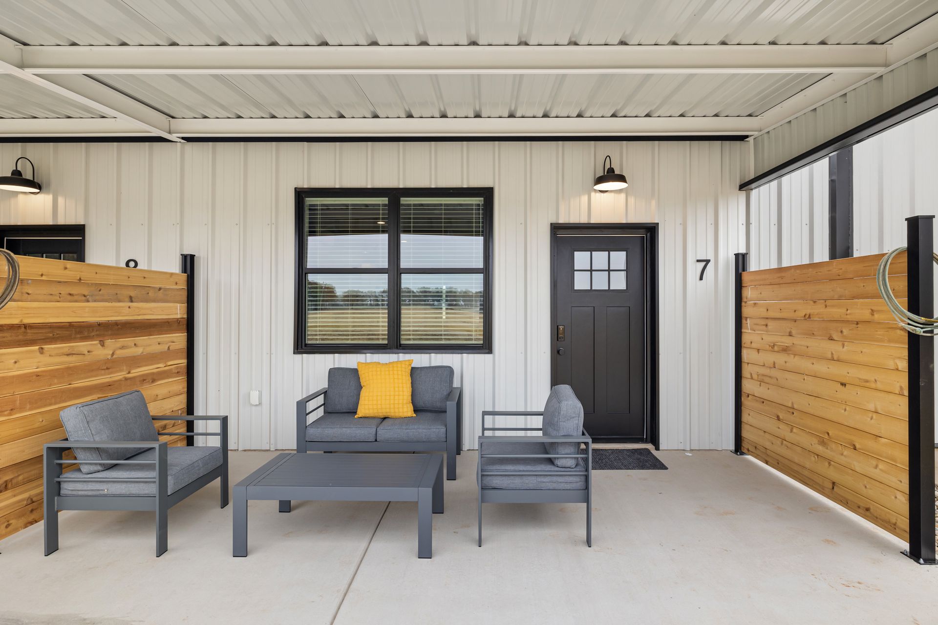 Covered patio with gray outdoor seating, wood privacy walls, and a black door and window.