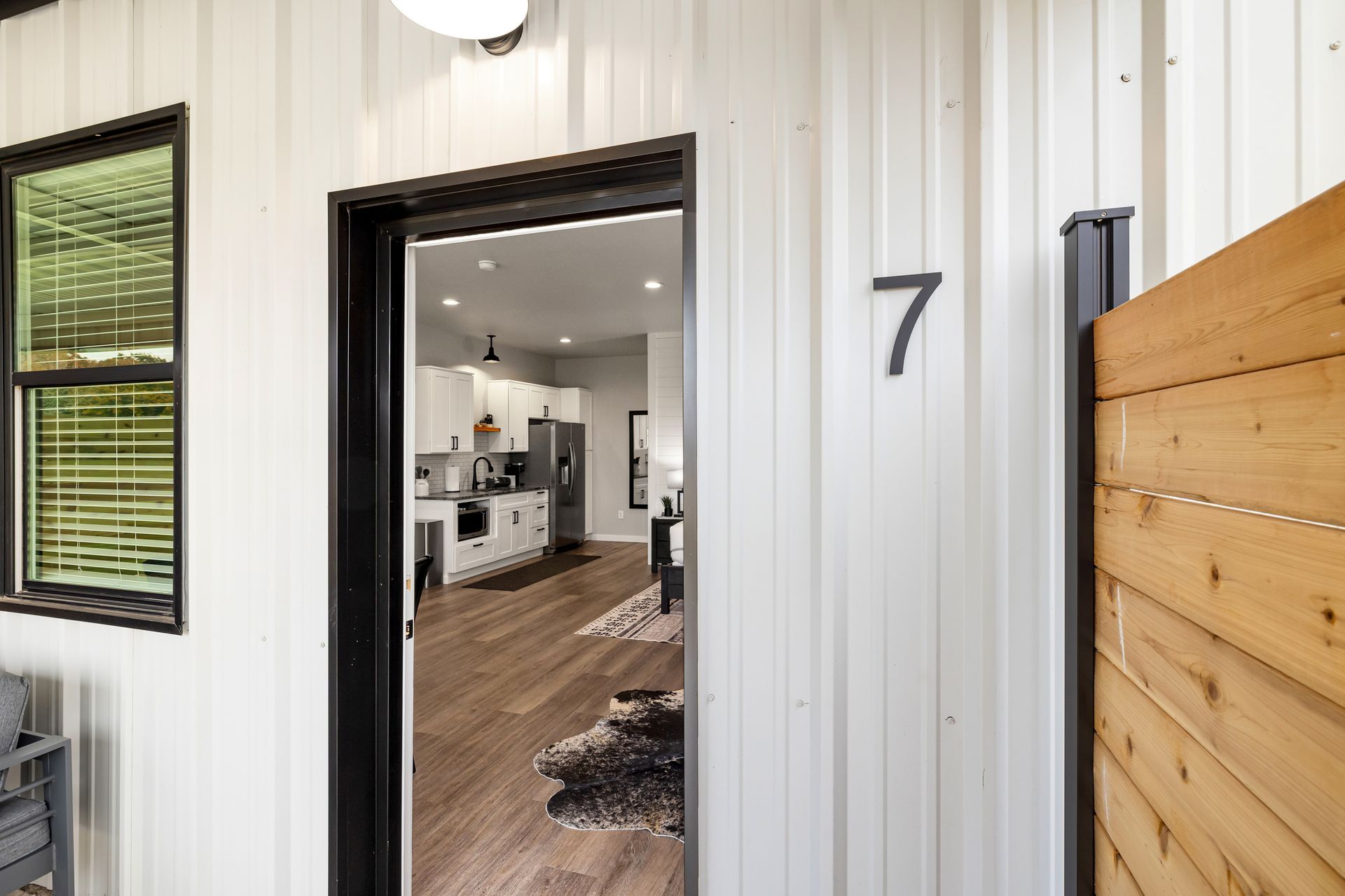 Front entry of a modern home with a black door, white siding, wood fence, and house number 7