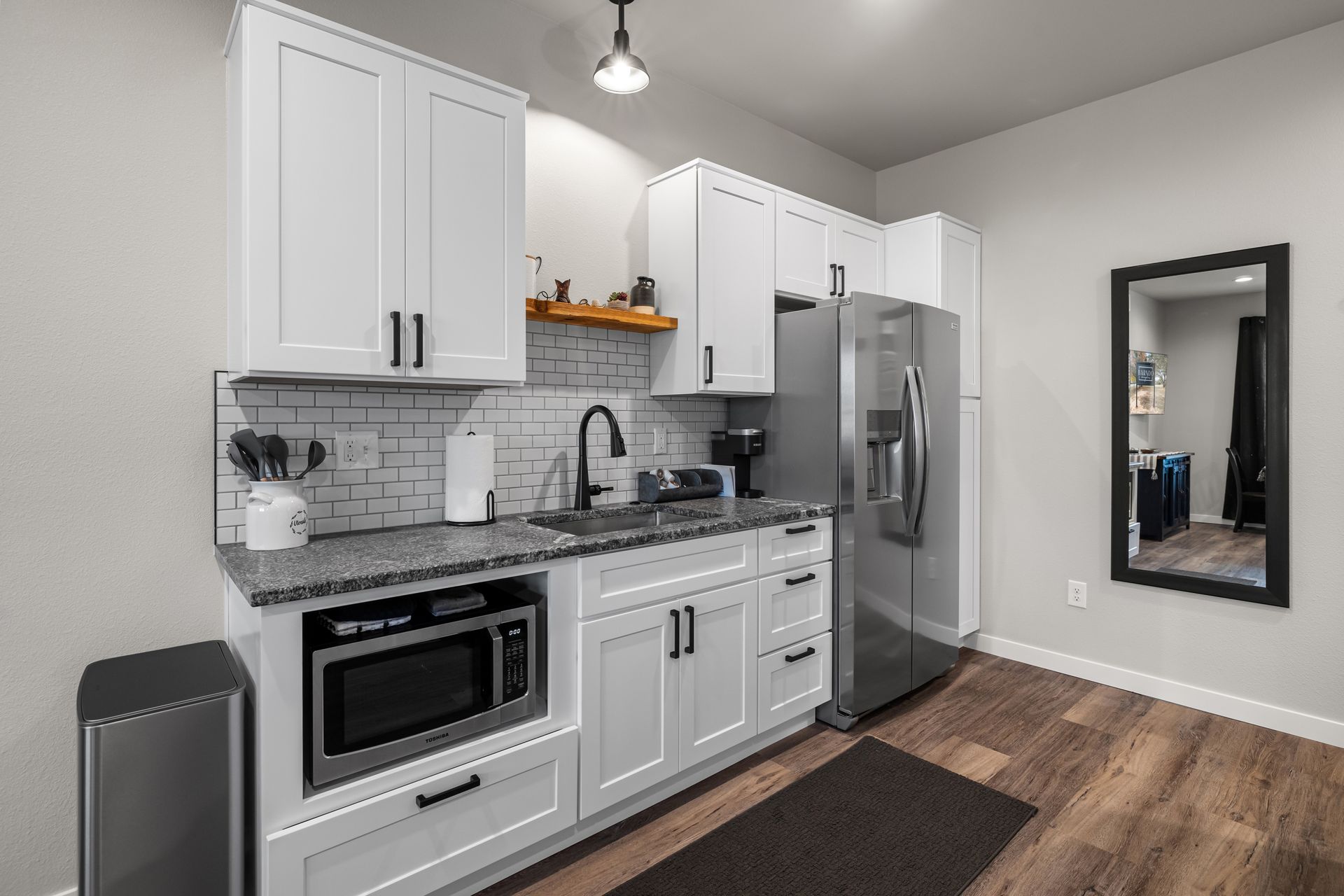 Modern kitchen with white cabinets, stainless appliances, granite counters, and wood-look flooring
